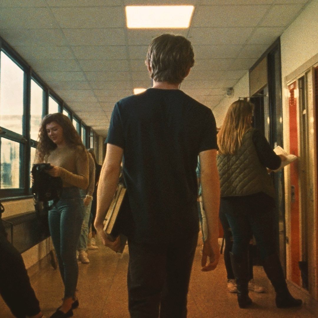 Students walking down a hallway with books in their hands - Austin Abrams