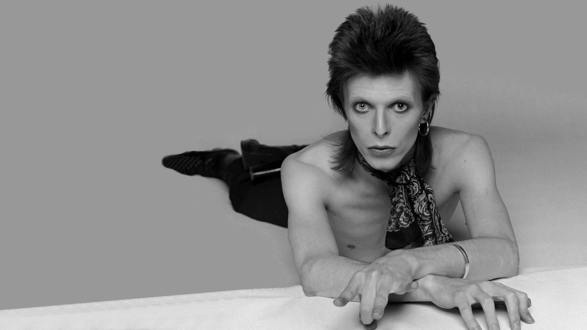 David Bowie, the Thin White Duke, poses shirtless in a black and white photo. - David Bowie