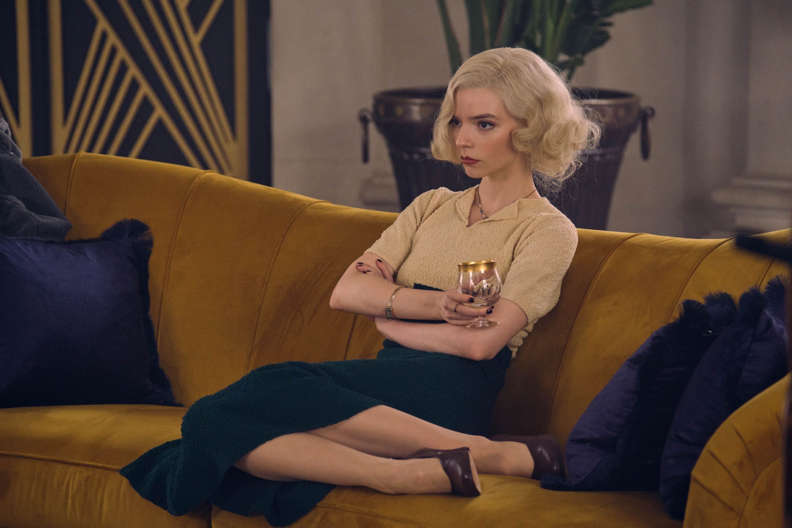 Holland Taylor as Elizabeth, a white woman with blonde hair, sits on a couch with her arms crossed and a glass of champagne in her hand. - Anya Taylor-Joy