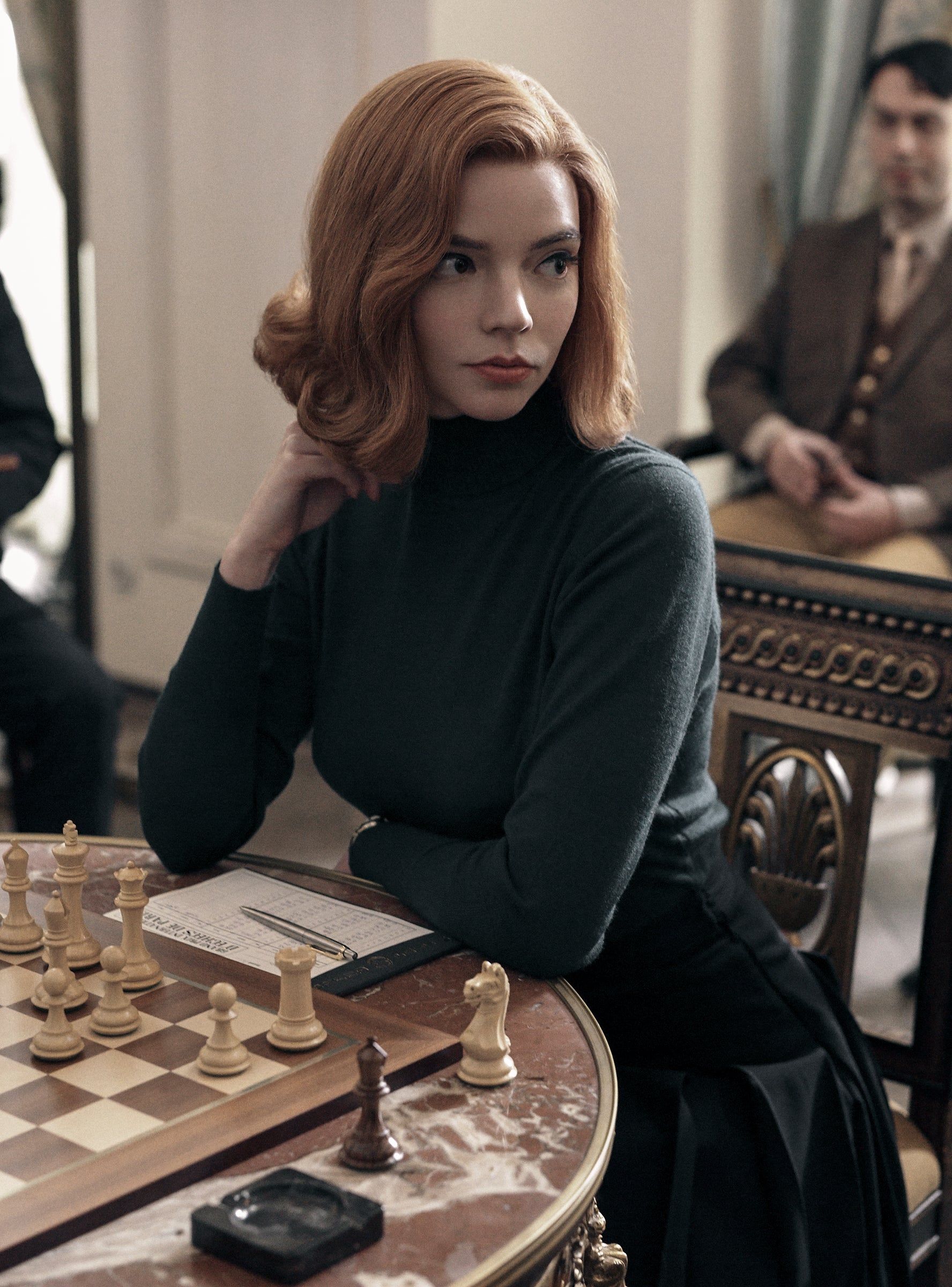 A woman with red hair sits at a table with a chess board. - Anya Taylor-Joy