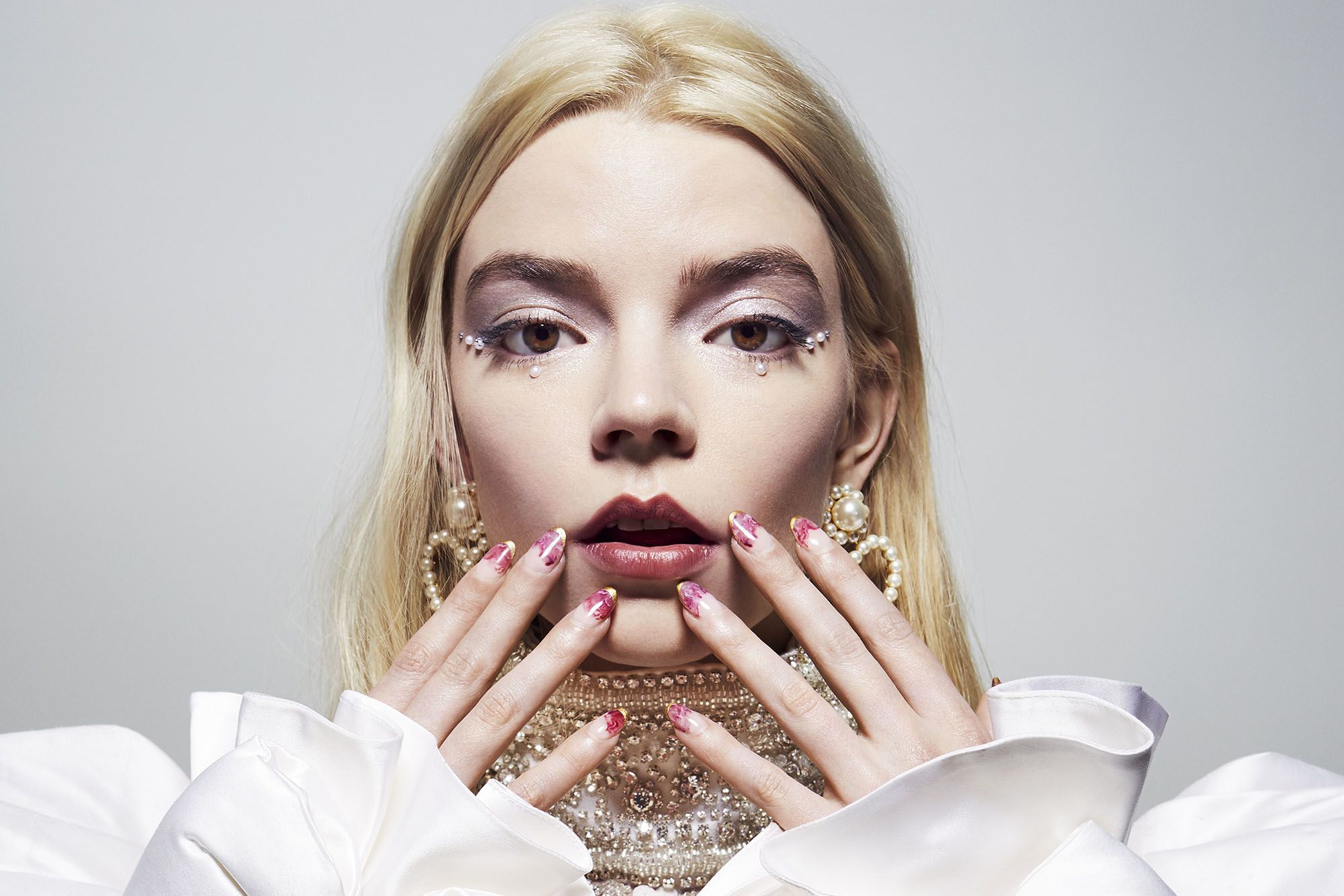 Pop artist Grimes wears a white top and gold jewelry with her hands on her face. - Anya Taylor-Joy