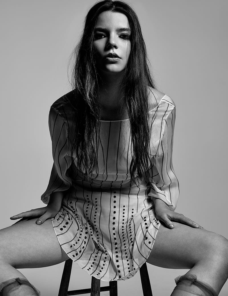 A woman sitting on a stool with a black and white striped dress - Anya Taylor-Joy