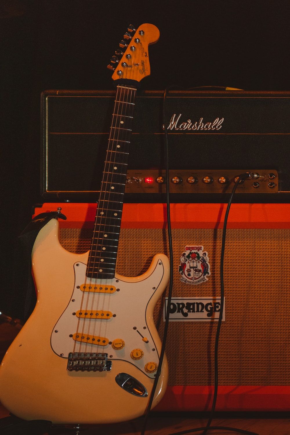 An electric guitar sits in front of two amplifiers. - Music