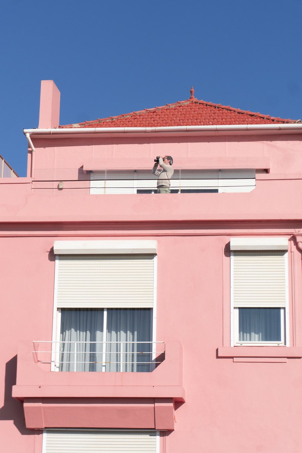 A man is taking a picture from the window of a pink building - Spotify