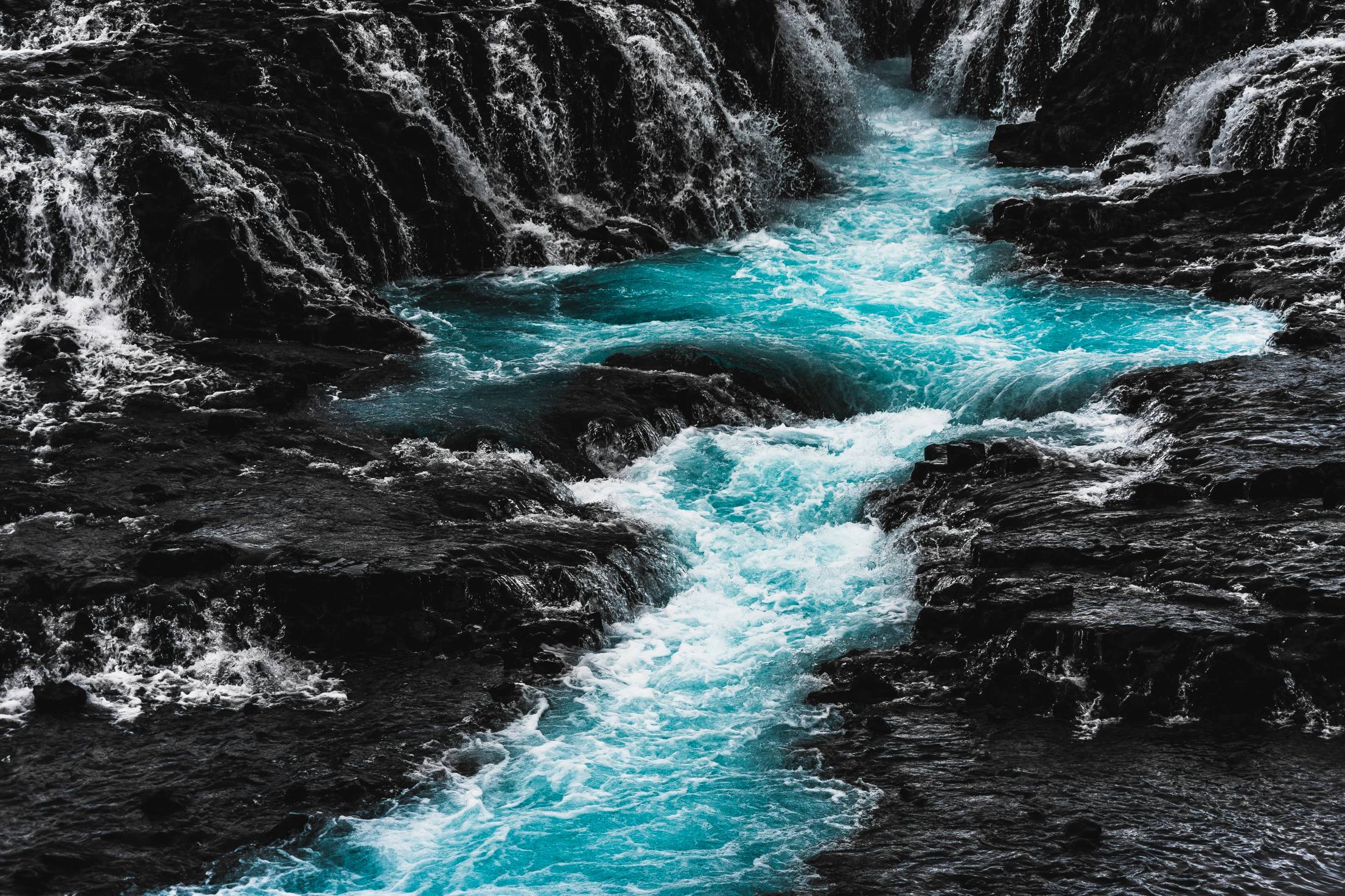 A river flows through rocks, the water is a beautiful shade of blue. - Waterfall