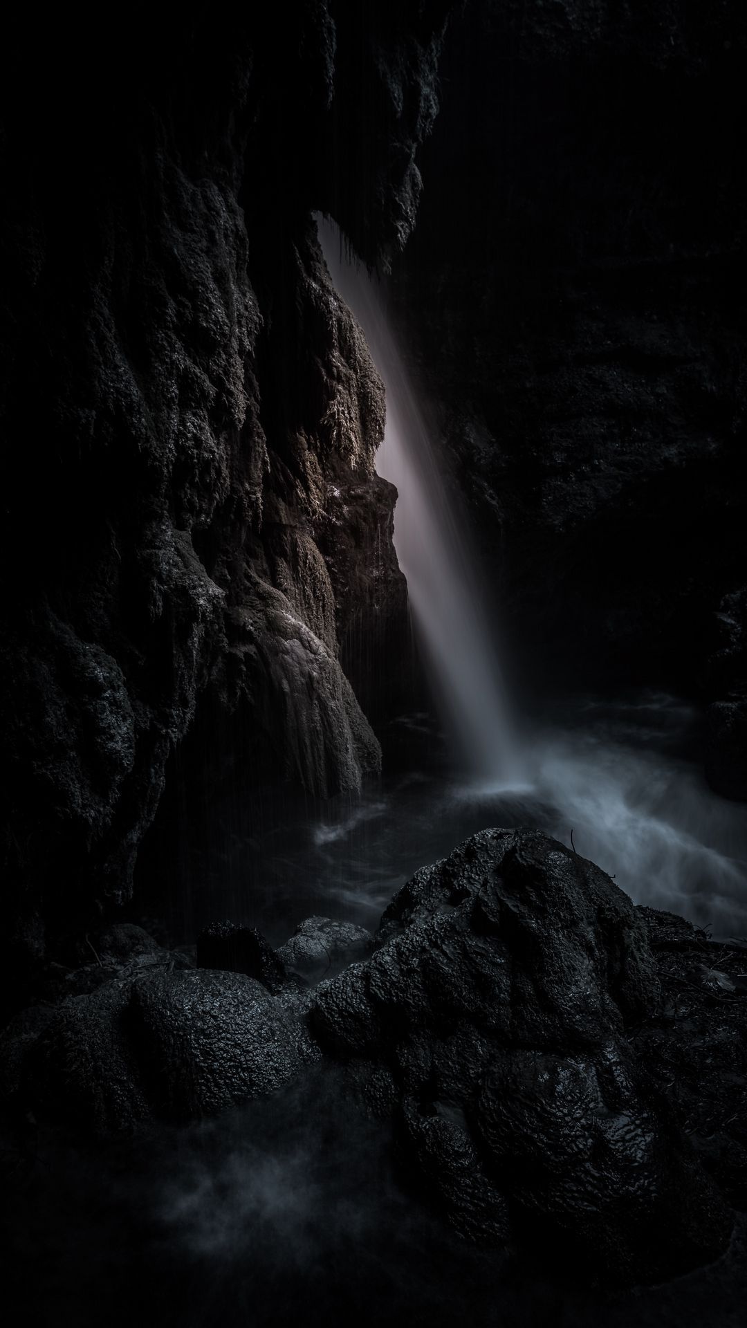 A waterfall cascading into a dark pool of water surrounded by rocks. - Waterfall