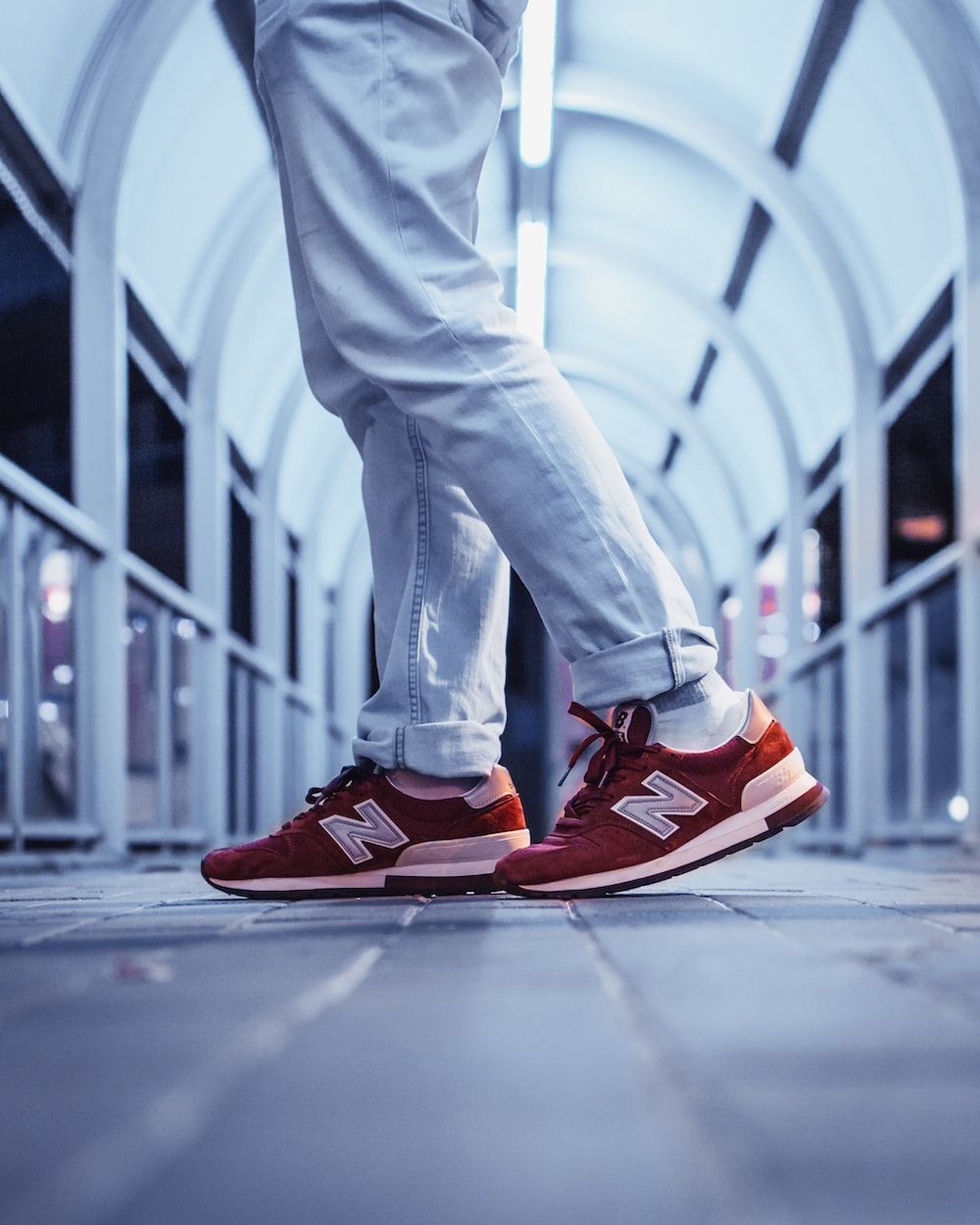 A person wearing a pair of red New Balance sneakers standing on a bridge. - New Balance