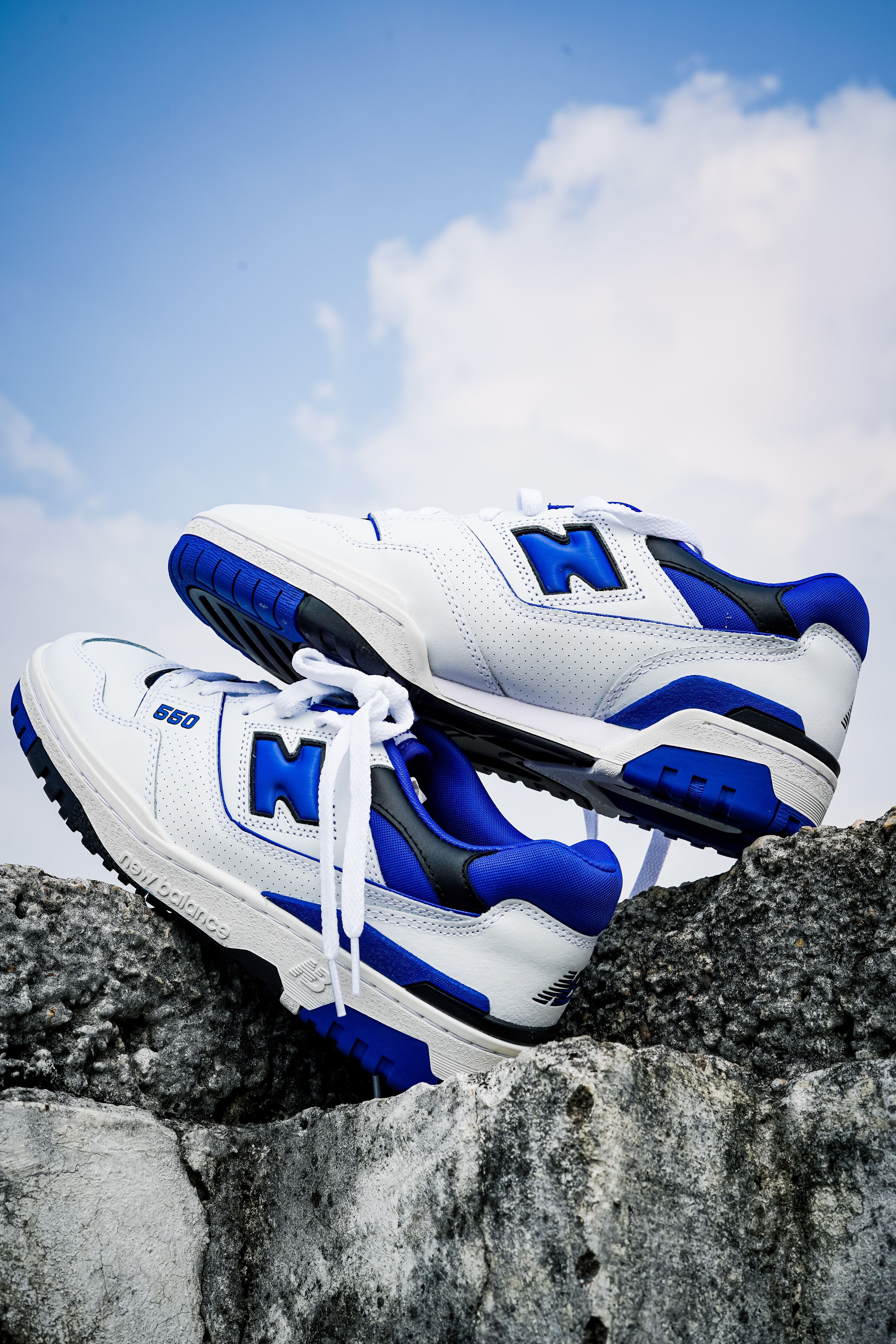 A pair of white and blue new balance sneakers on a rock - New Balance