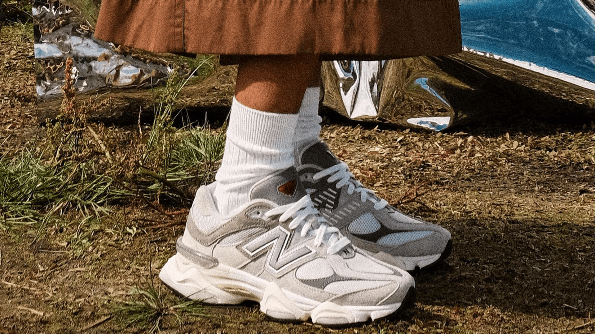 A person wearing a brown skirt and white socks with white and grey chunky sneakers. - New Balance