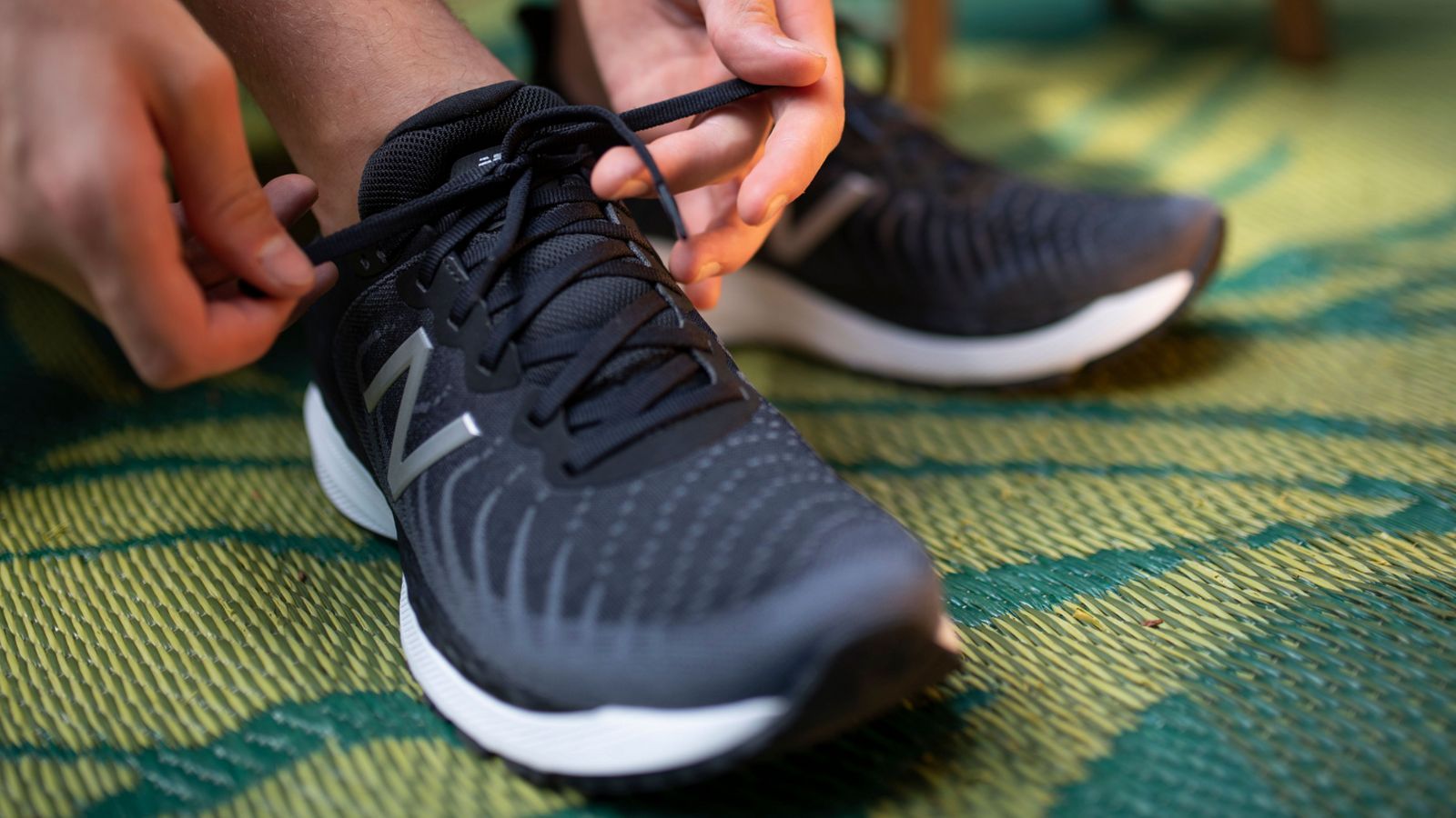 A person tying the laces on a pair of black New Balance sneakers. - New Balance