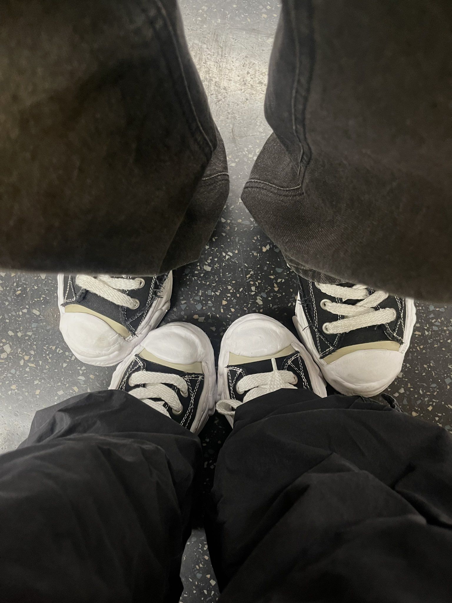 A photo of two pairs of feet in black and white converse sneakers. - Converse