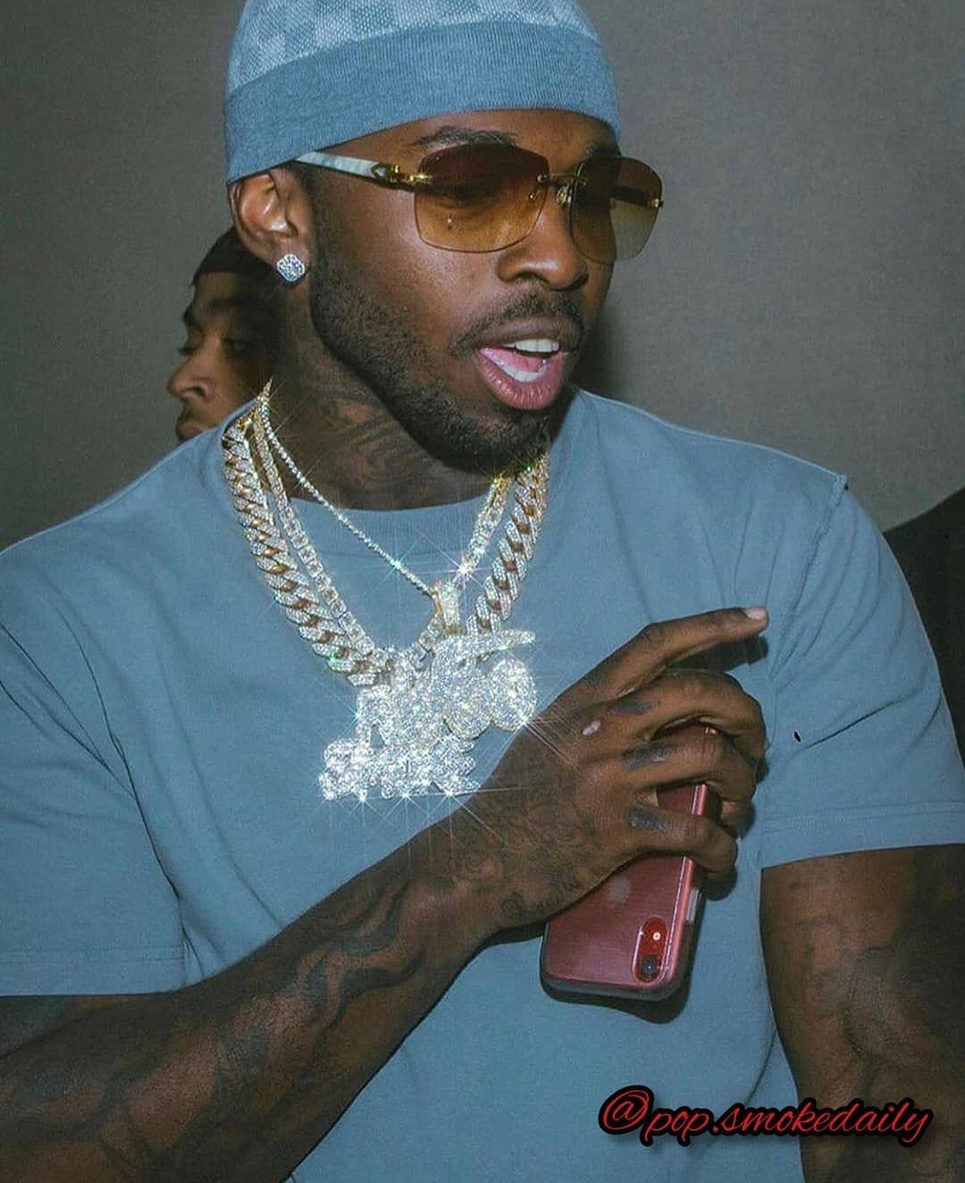Rapper YFN Lucci in a blue shirt and a blue hat holding a red iPhone - Pop Smoke