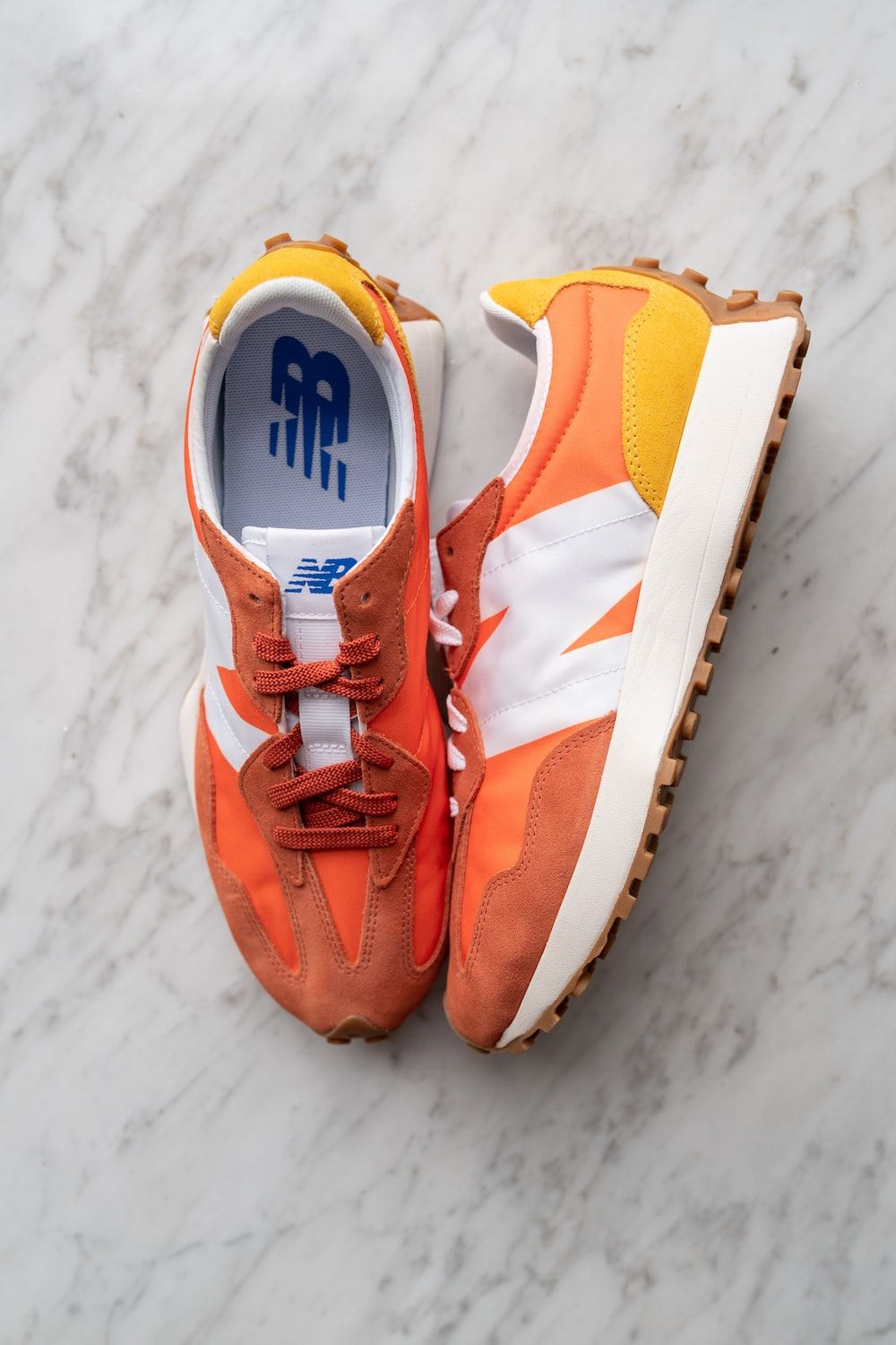 An orange and white New Balance sneakers on a marble surface - New Balance