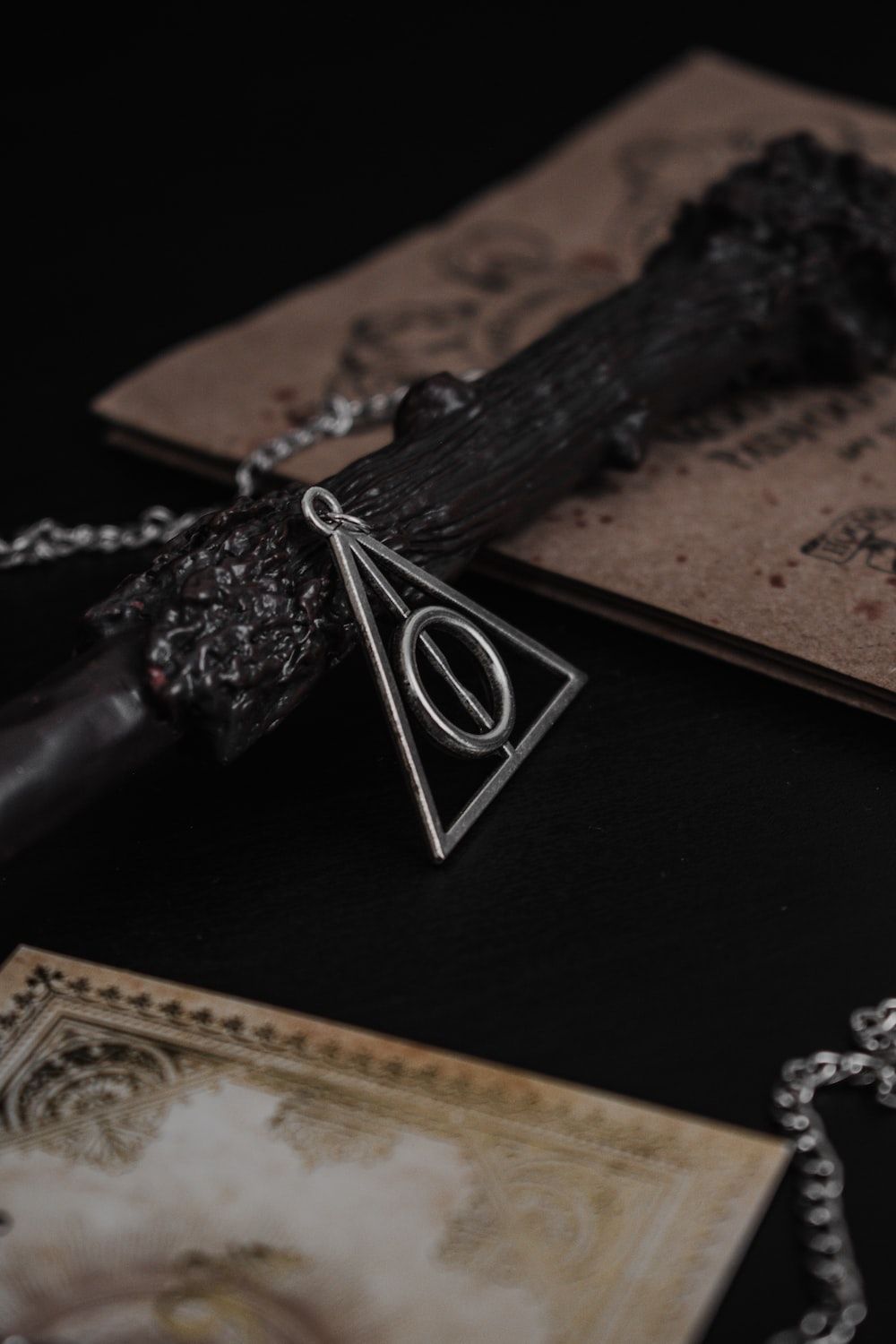 A Deathly Hallows necklace on a table with a wand and a book. - Harry Potter