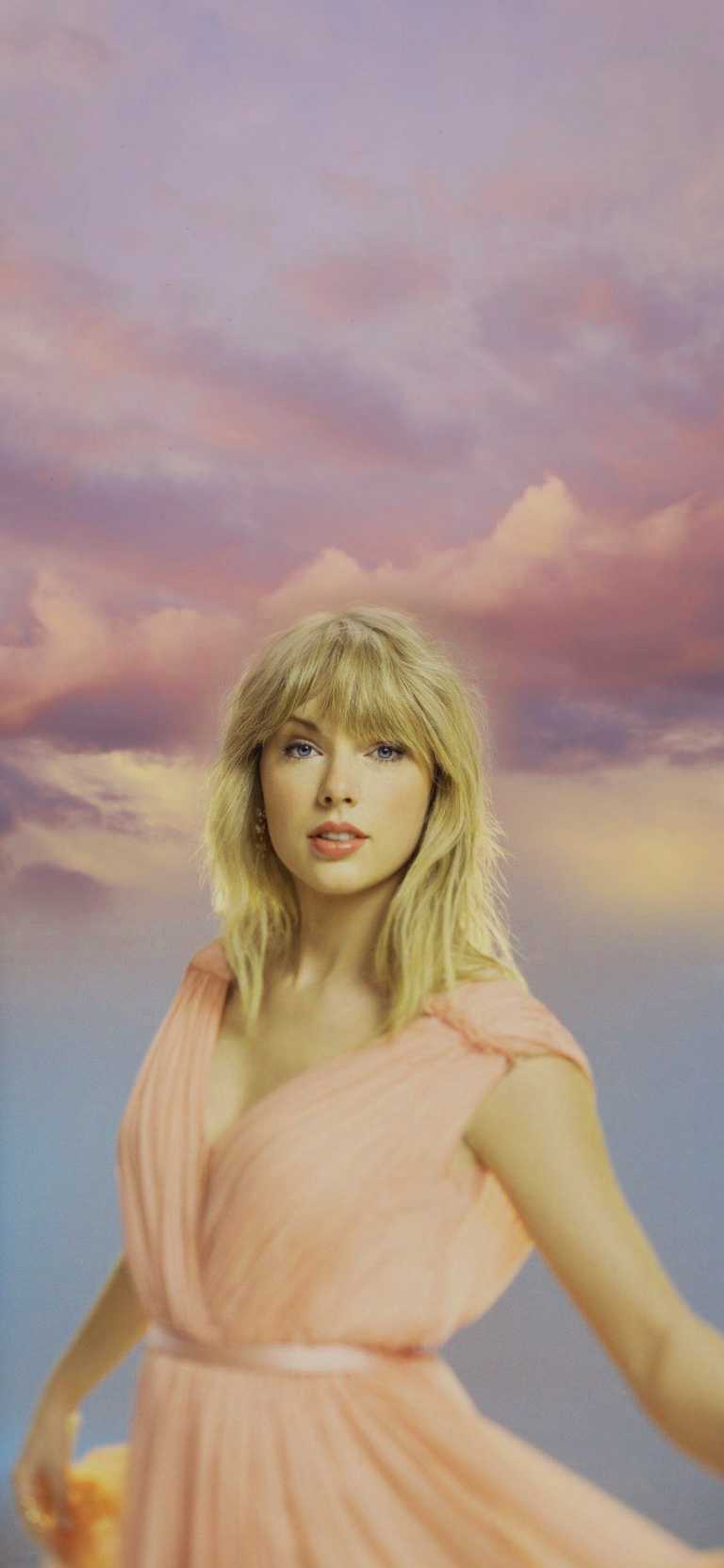 Taylor Swift in a pink dress standing in front of a pink sky - Taylor Swift