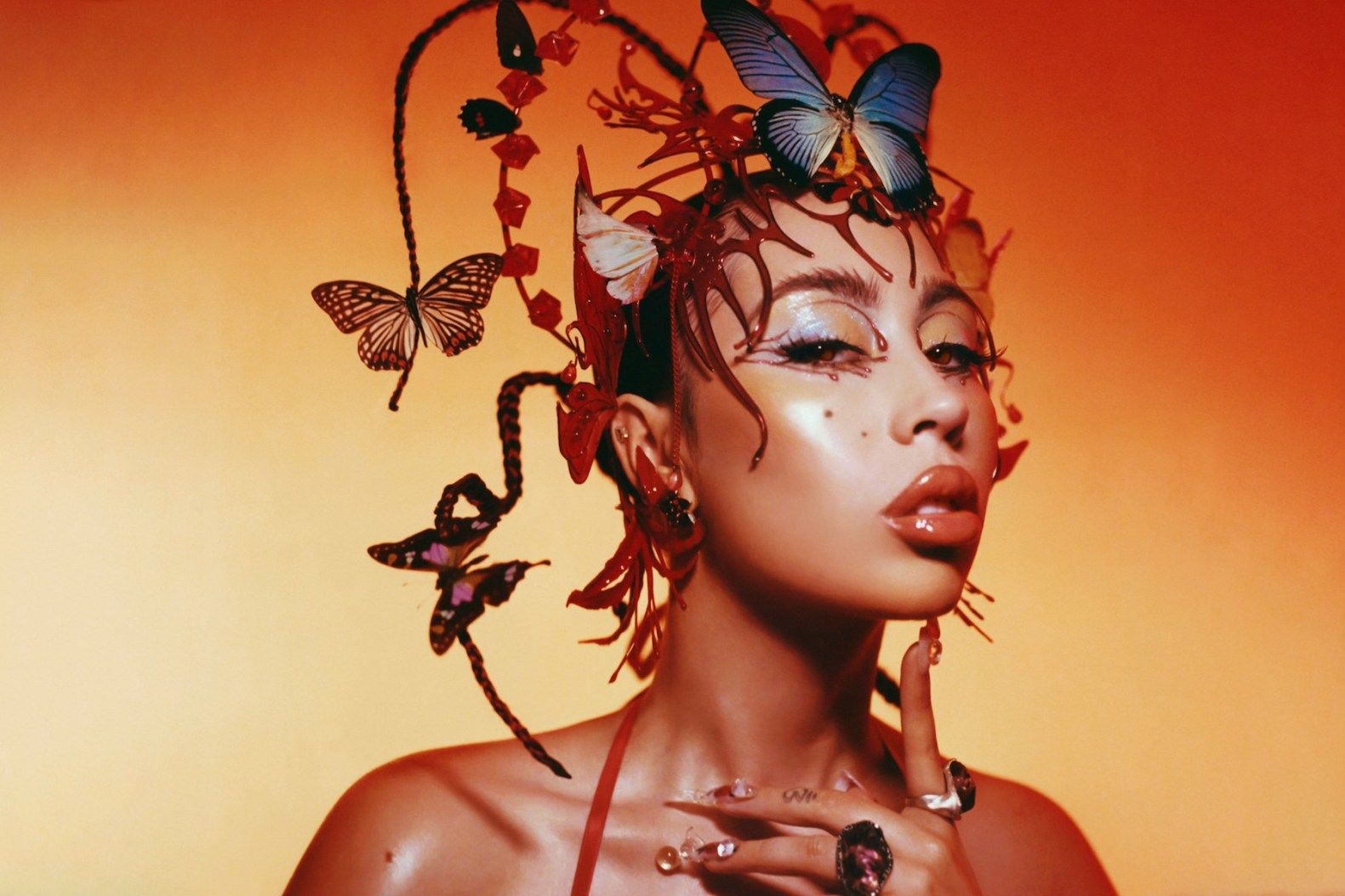 A woman with butterflies on her head and orange background - Kali Uchis