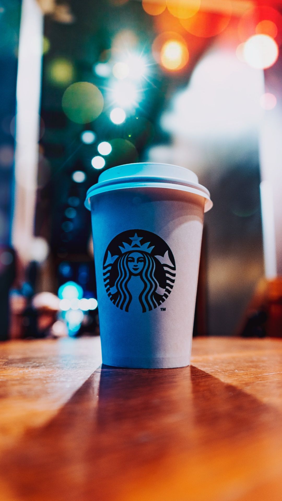 A Starbucks cup on a table with a blurred background - Starbucks