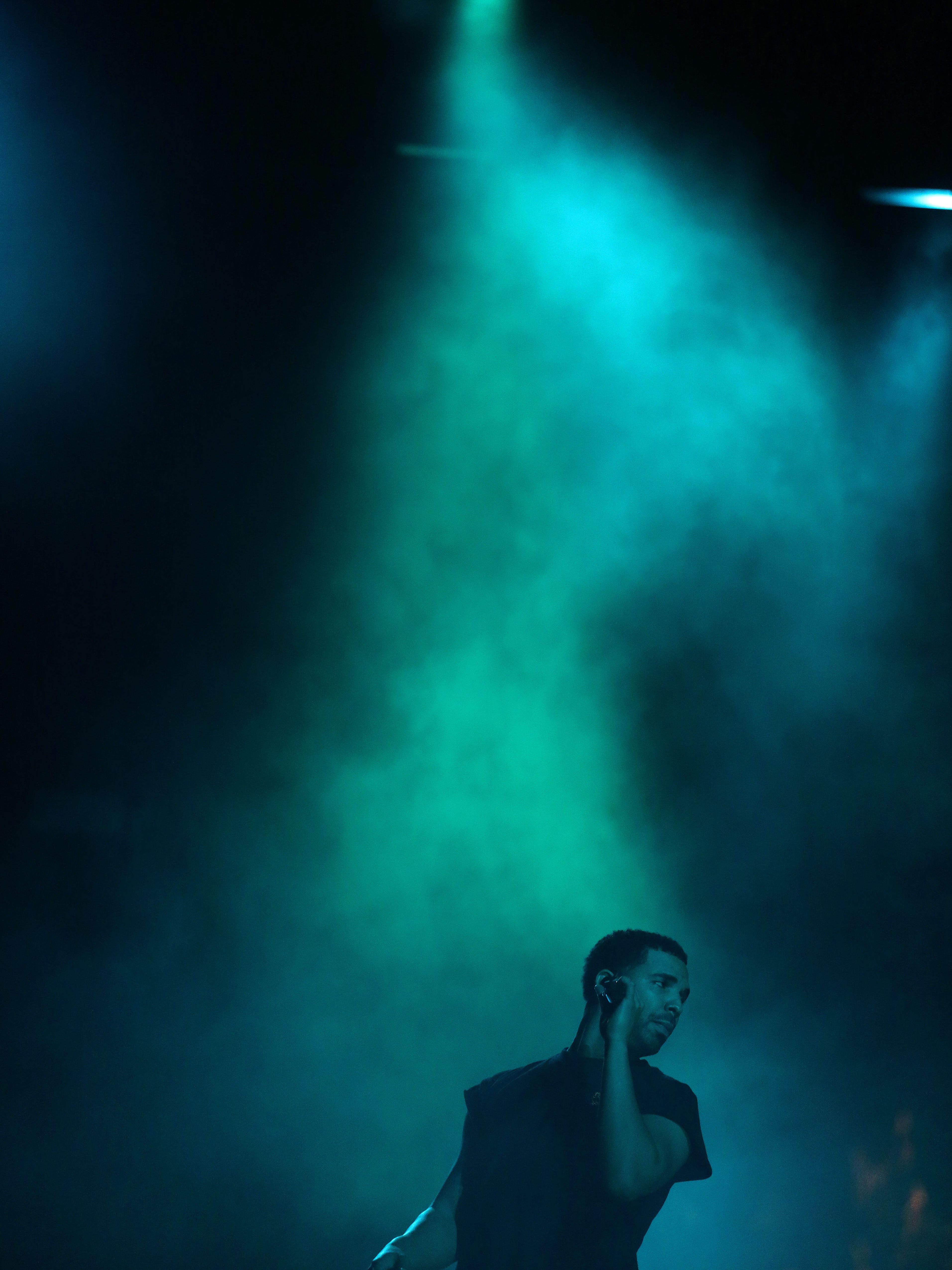 A man standing under a blue light with smoke - Drake