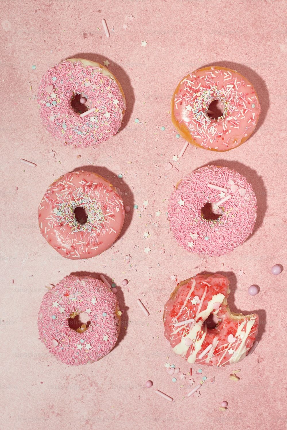 A pink background with six pink donuts with sprinkles on them. - Blush