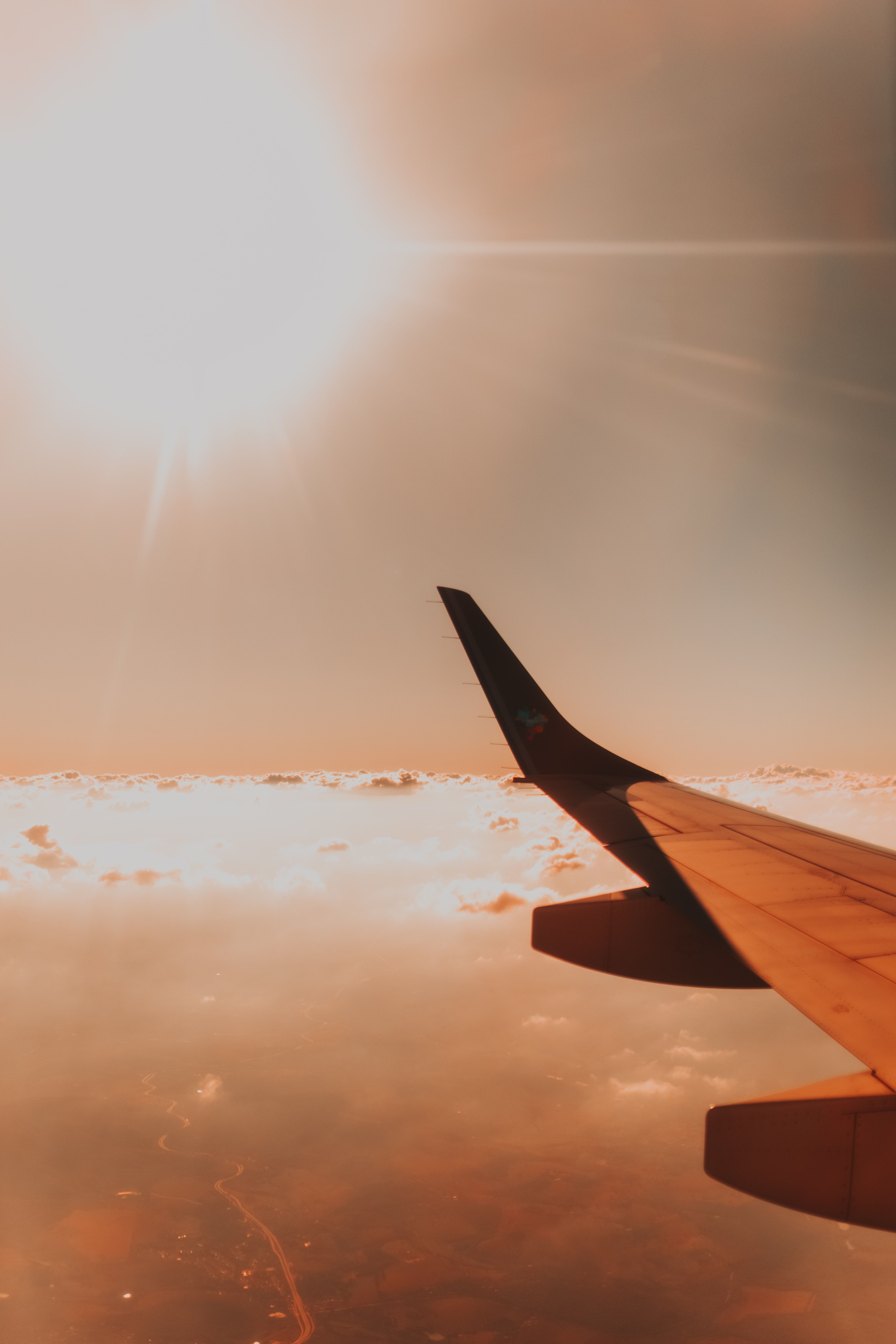 An airplane wing above the clouds against a bright sun. - Airplane