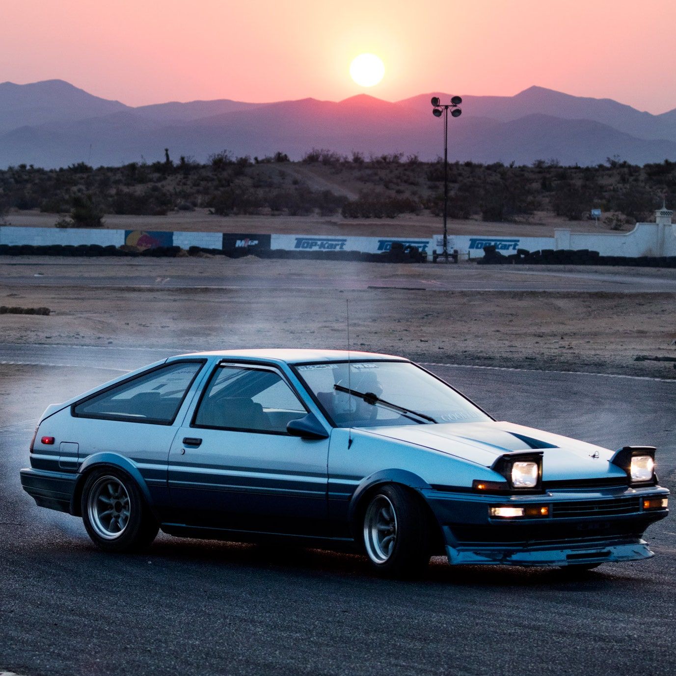 A car driving on a track with the sun setting in the background. - Toyota AE86