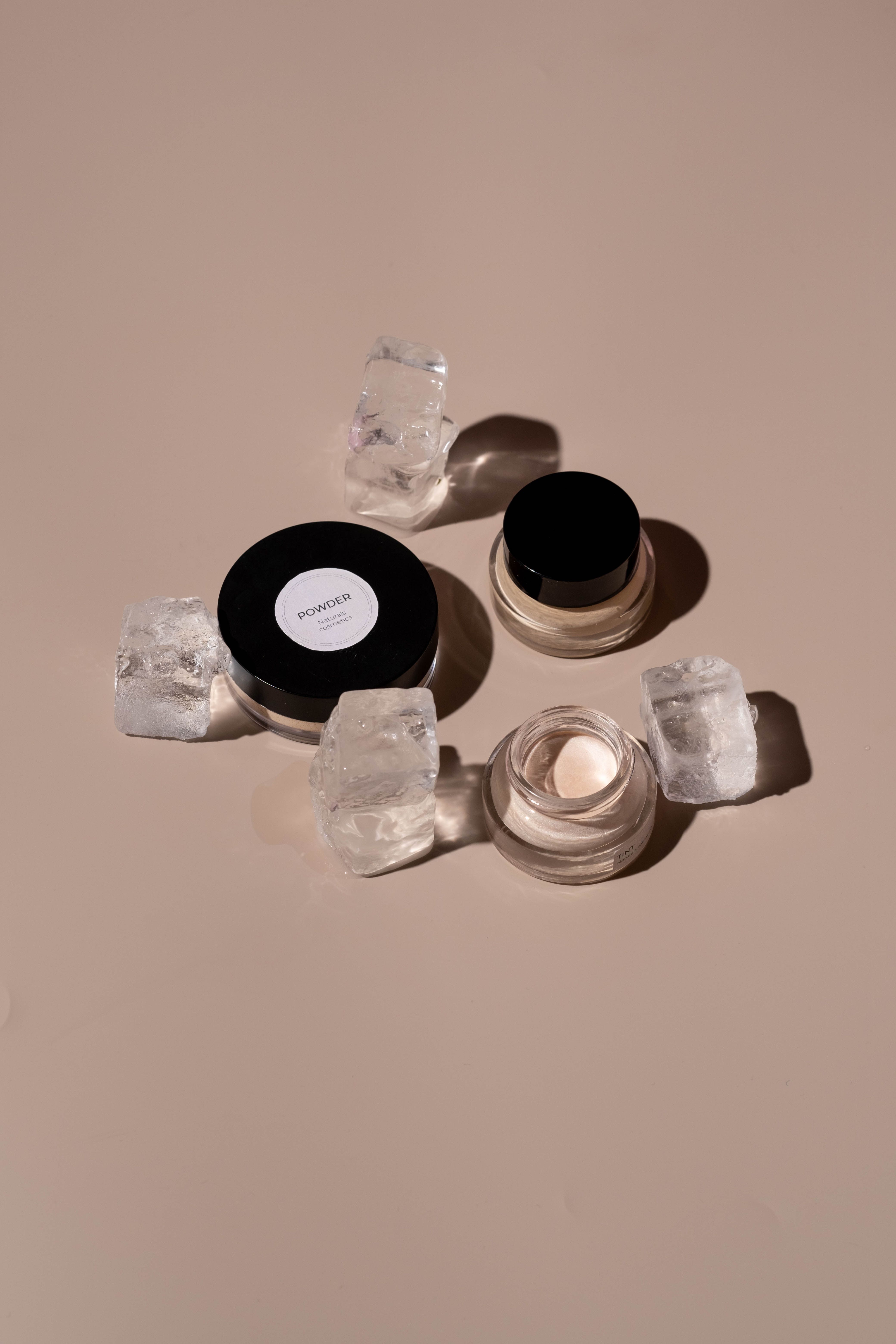 Two open jars of cream surrounded by ice cubes on a beige background - Makeup