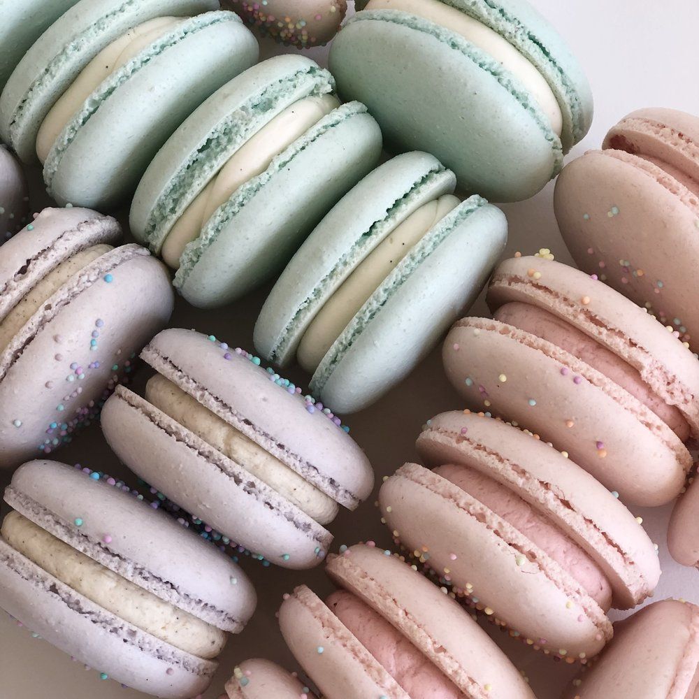 A plate of macarons with pastel colors and sprinkles on top. - Macarons