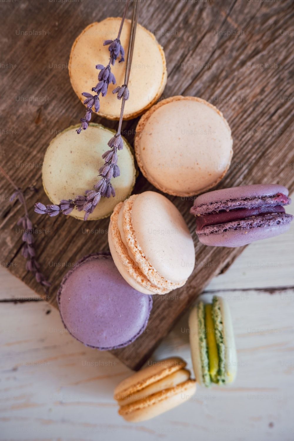 Aerial view of a variety of macarons on a wooden board with a sprig of lavender. - Macarons