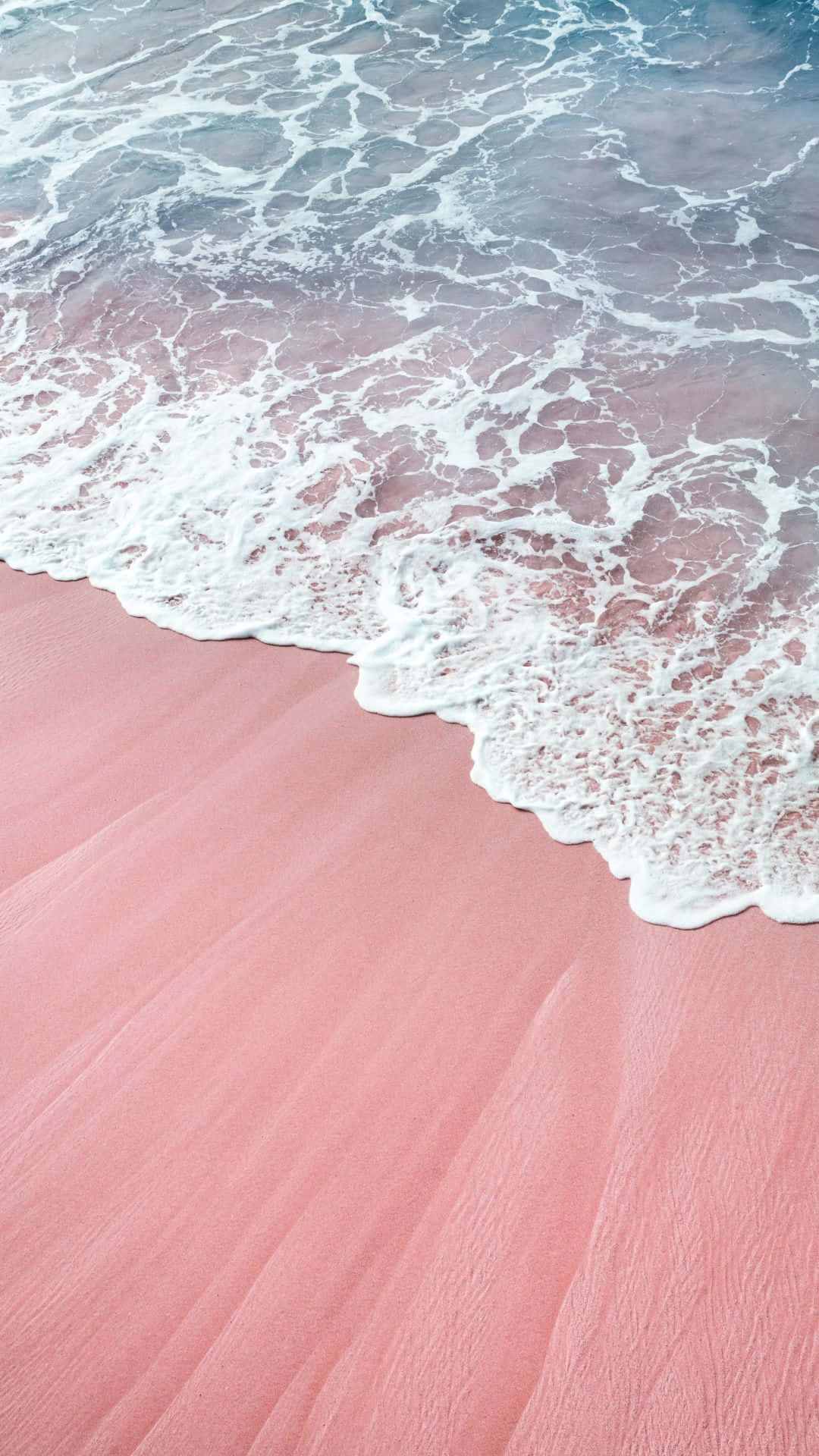 A pink sand beach with a white wave coming in. - Sand
