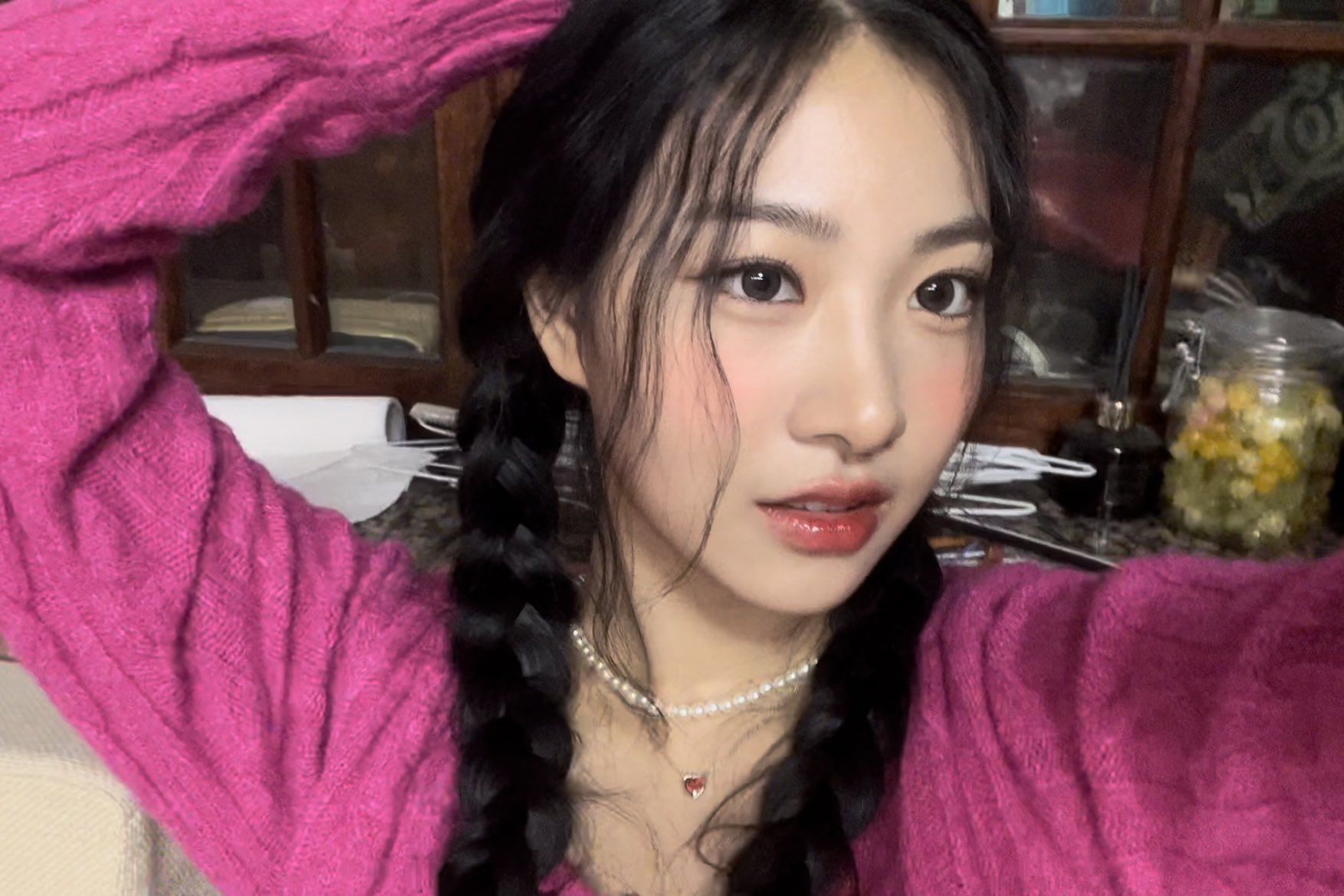 A selfie of a woman with long dark hair, wearing a pink knitted sweater and a pearl necklace. - FIFTY FIFTY