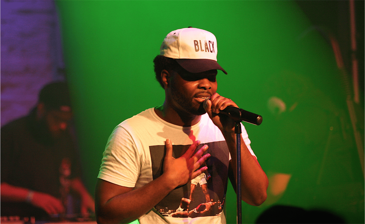 A man in a white hat singing into a microphone. - Chance the Rapper