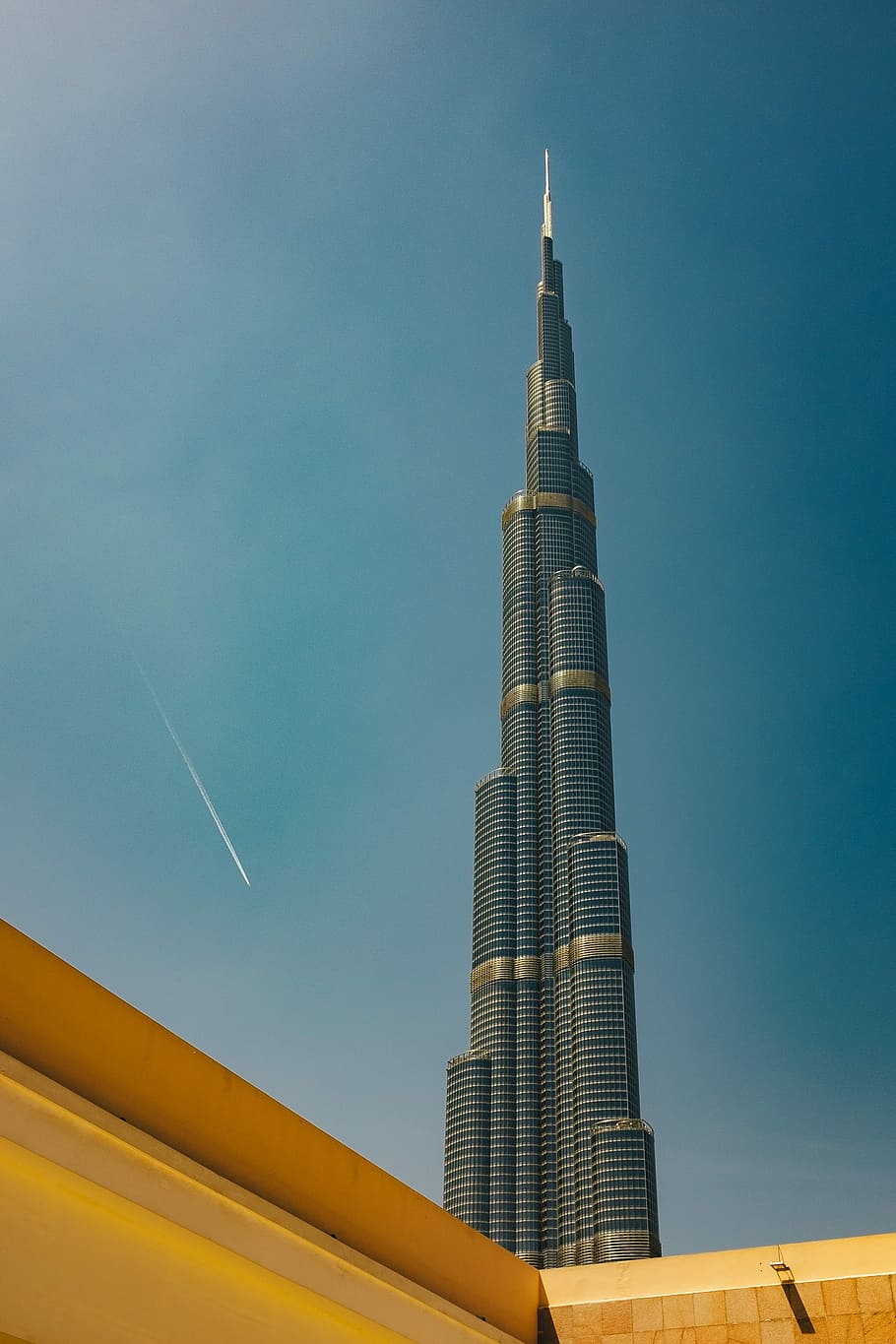 A tall building with a plane flying by in the sky. - Dubai