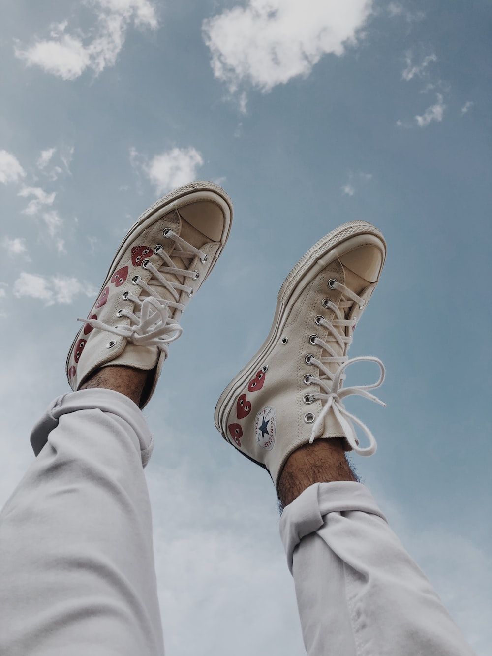 A person wearing white Converse sneakers with red and blue hearts on it. - Converse, shoes, sky