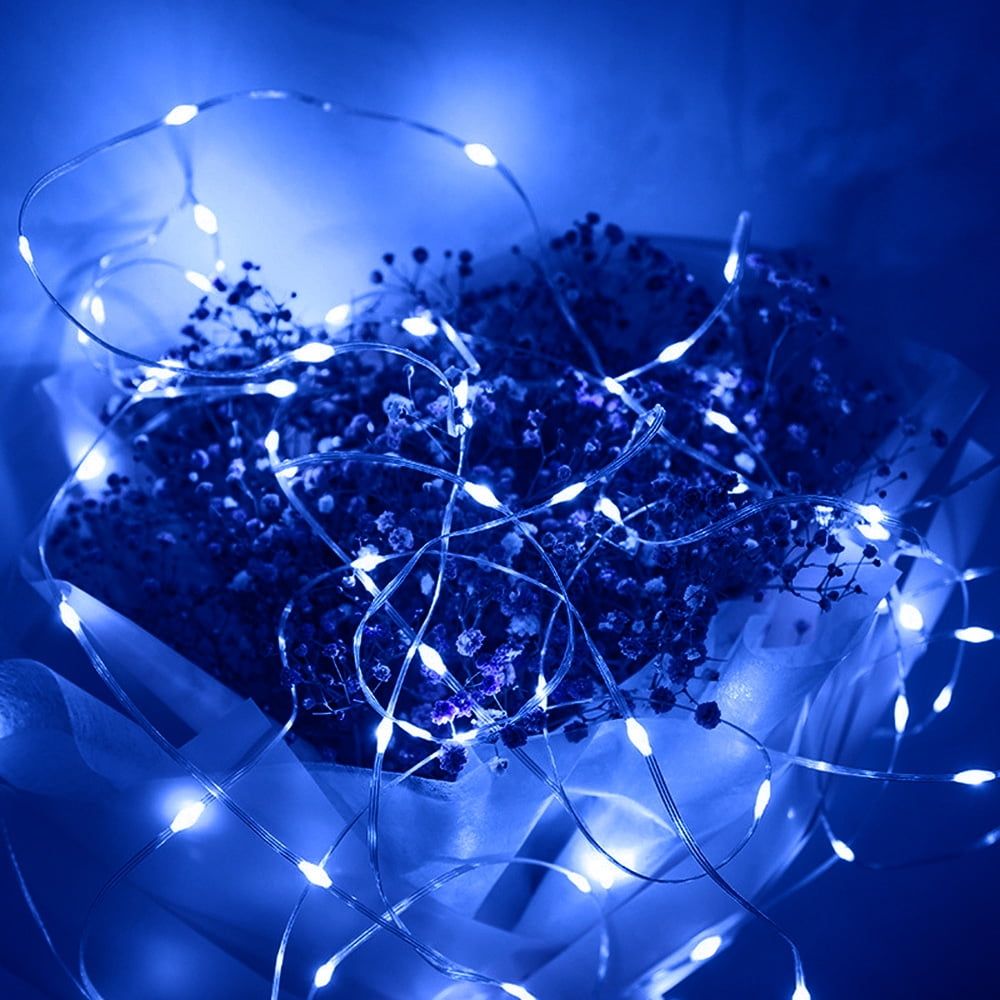A bouquet of blue flowers wrapped in white paper and string lights. - Fairy lights
