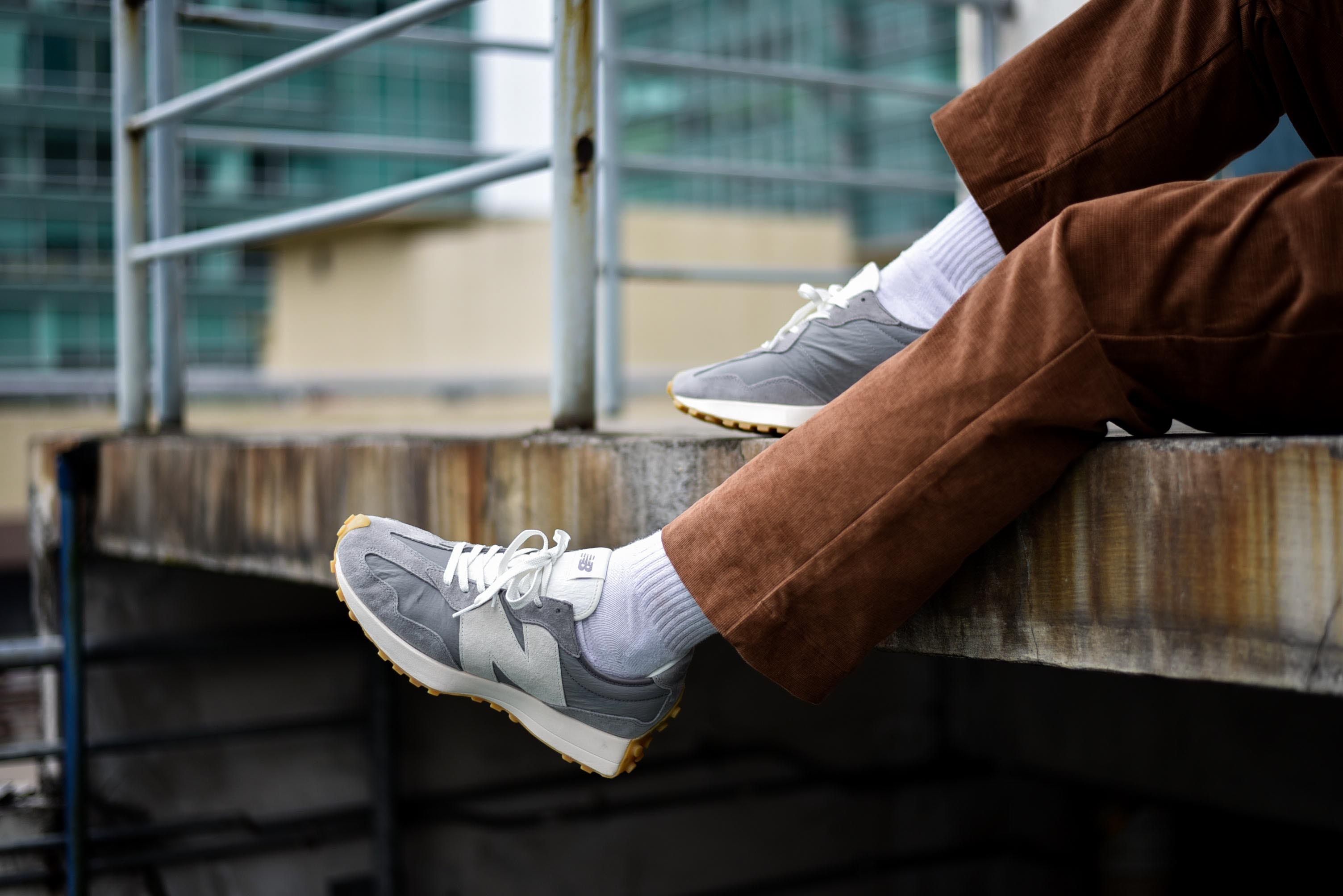 A person wearing New Balance 327 sneakers sitting on a ledge - New Balance