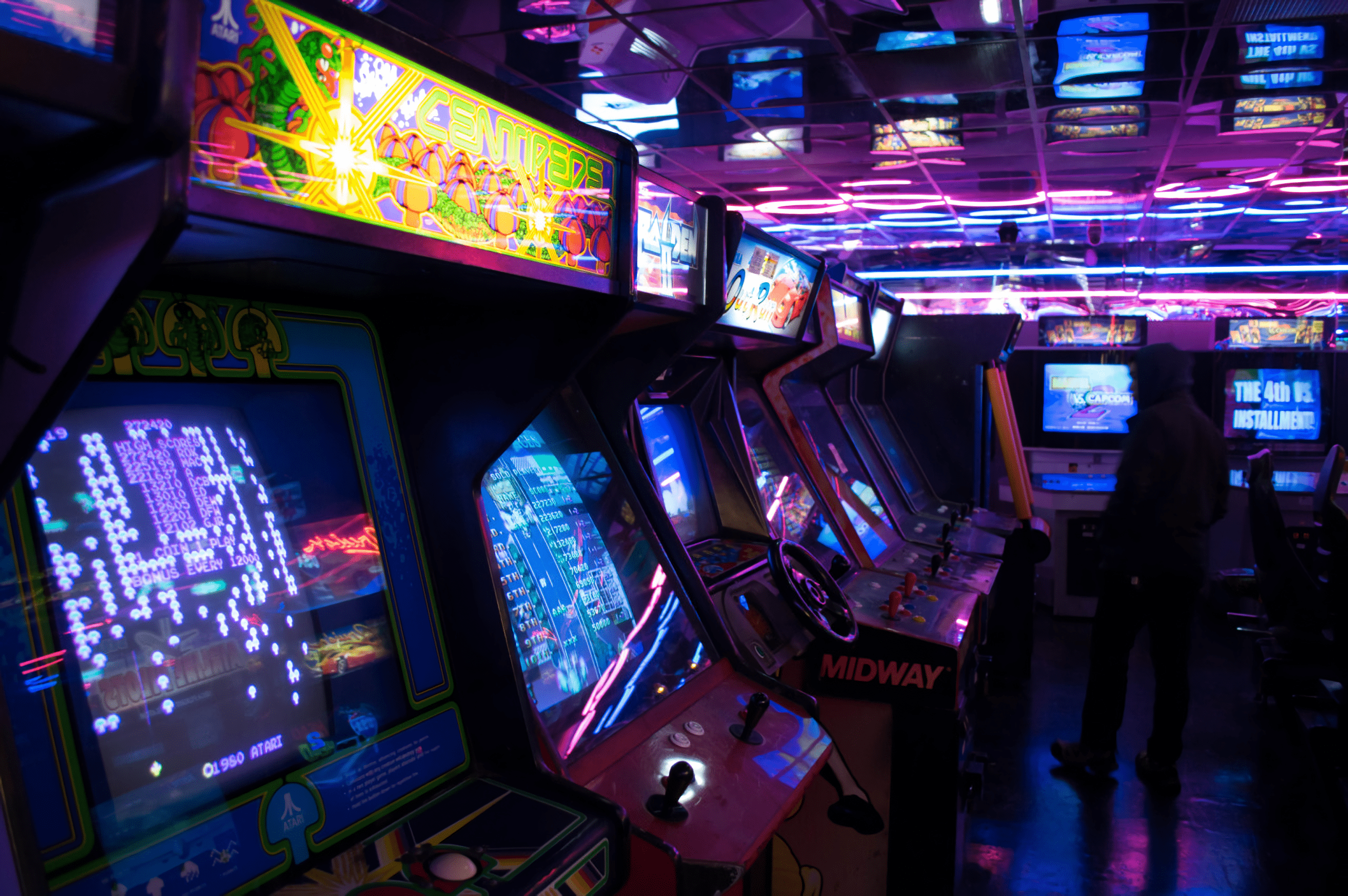A row of video games are lit up with purple and pink lights. - Arcade