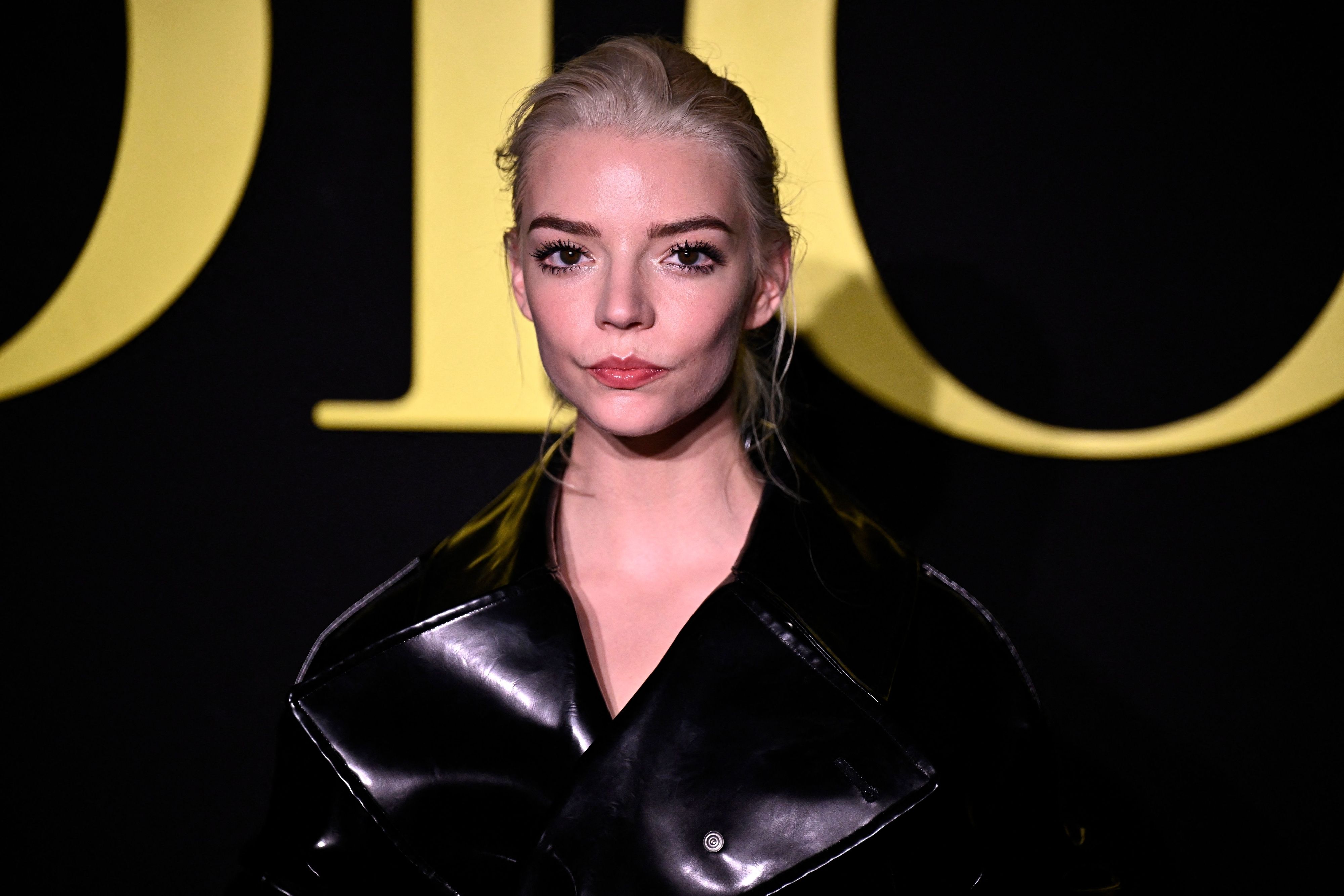 Anya Taylor-Joy poses in a leather jacket in front of a Dior sign - Anya Taylor-Joy