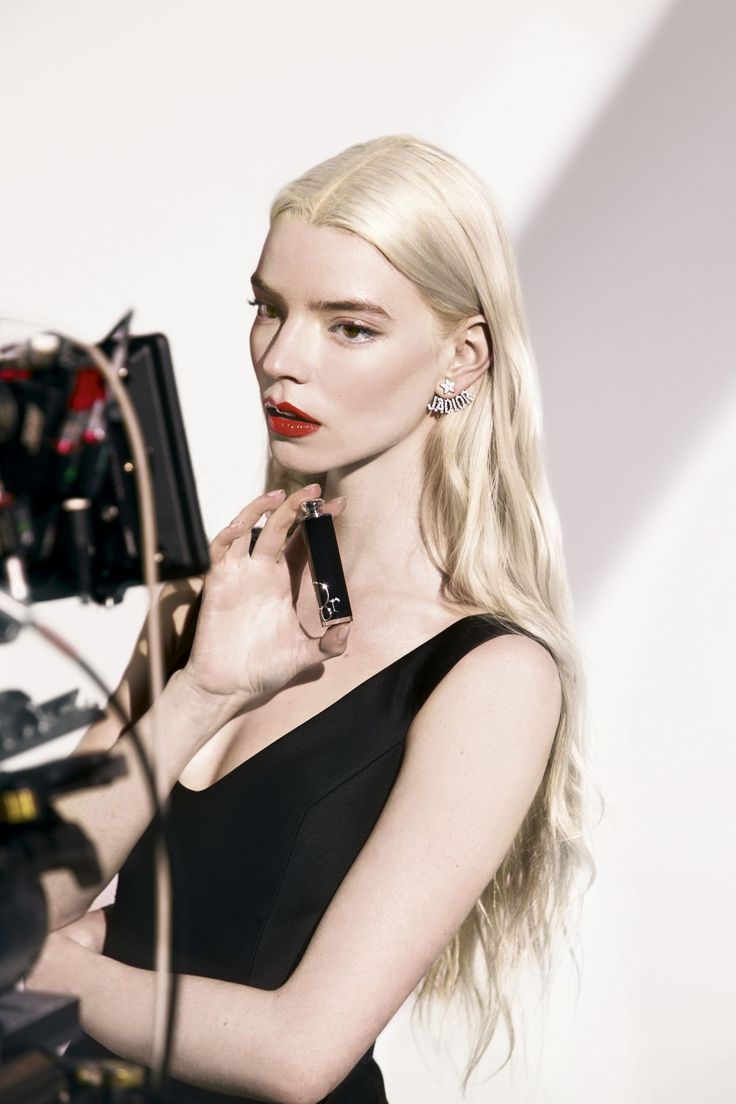 A model with long blonde hair and red lipstick holds a Dior lipstick - Anya Taylor-Joy