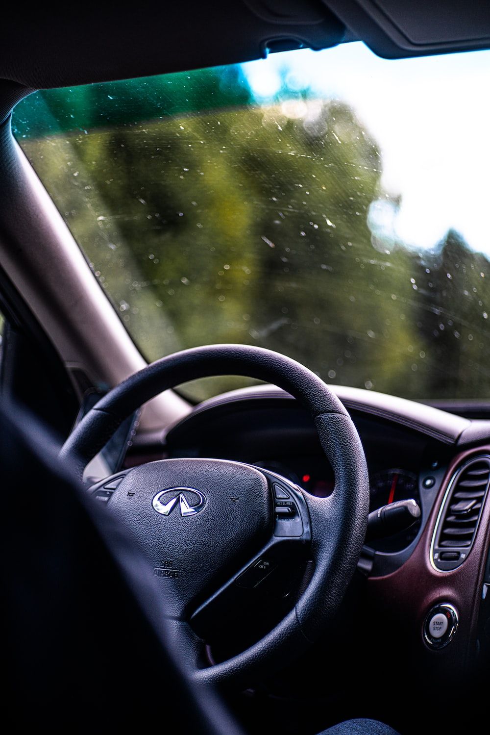 A car's steering wheel and dashboard, with raindrops visible on the windshield - Cars