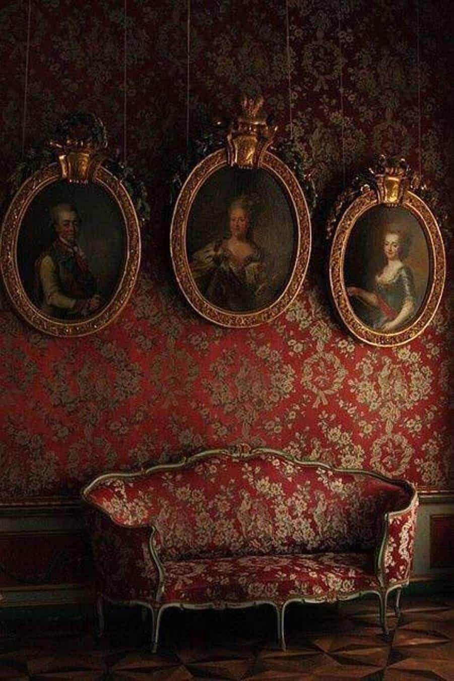 A red couch sits below three portraits in gold frames. - Victorian