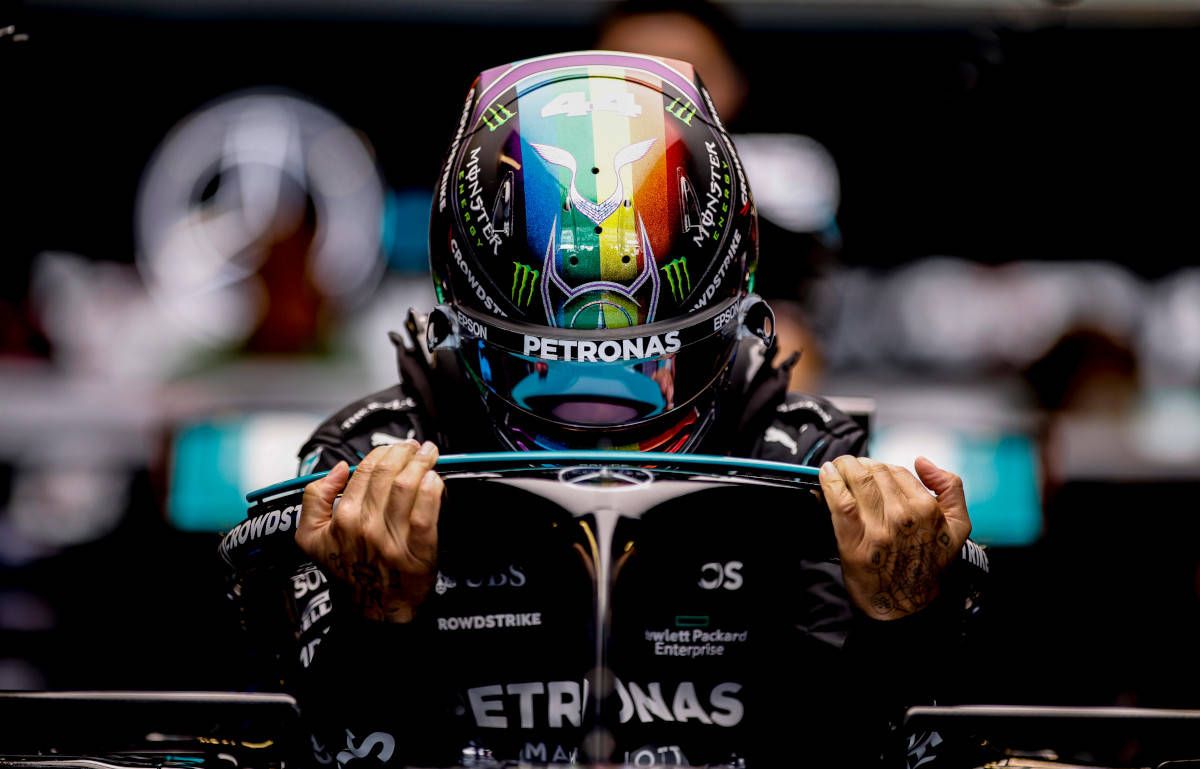 Lewis Hamilton with his helmet on, holding the steering wheel of his car - Lewis Hamilton