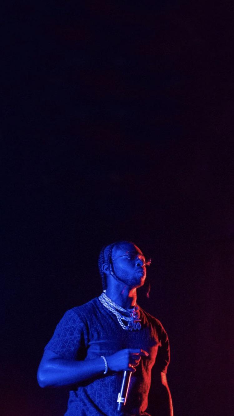Travis Scott holding a microphone in a blue room - Pop Smoke