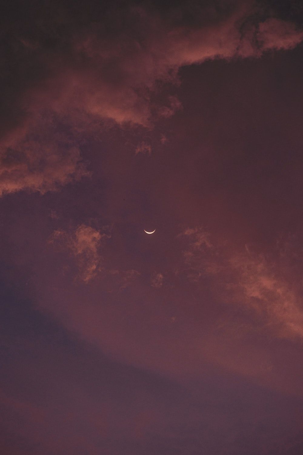 A crescent moon peeks through the clouds during a purple sunset. - HD