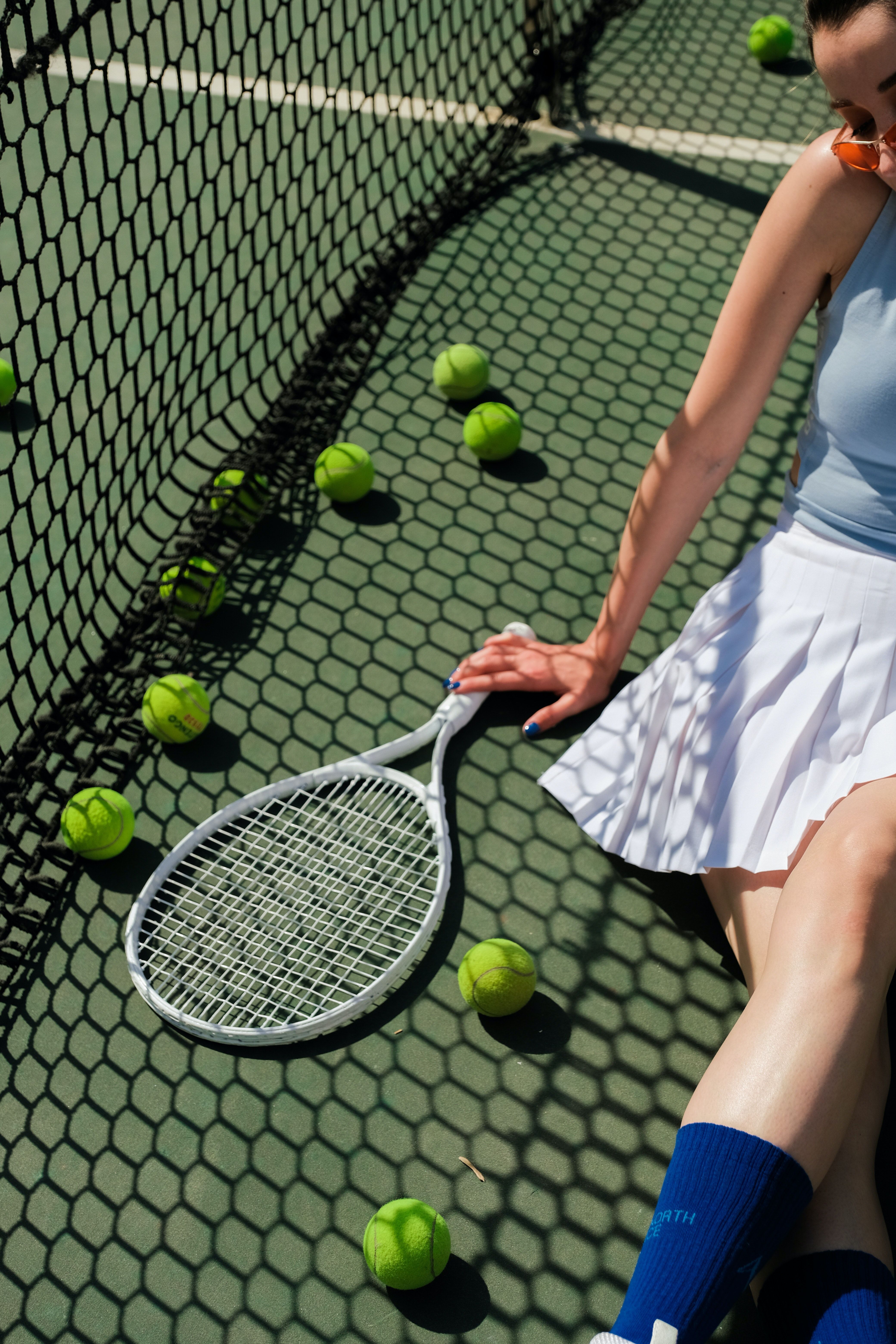 A woman is sitting on the ground with a tennis racket in her hand. - Tennis