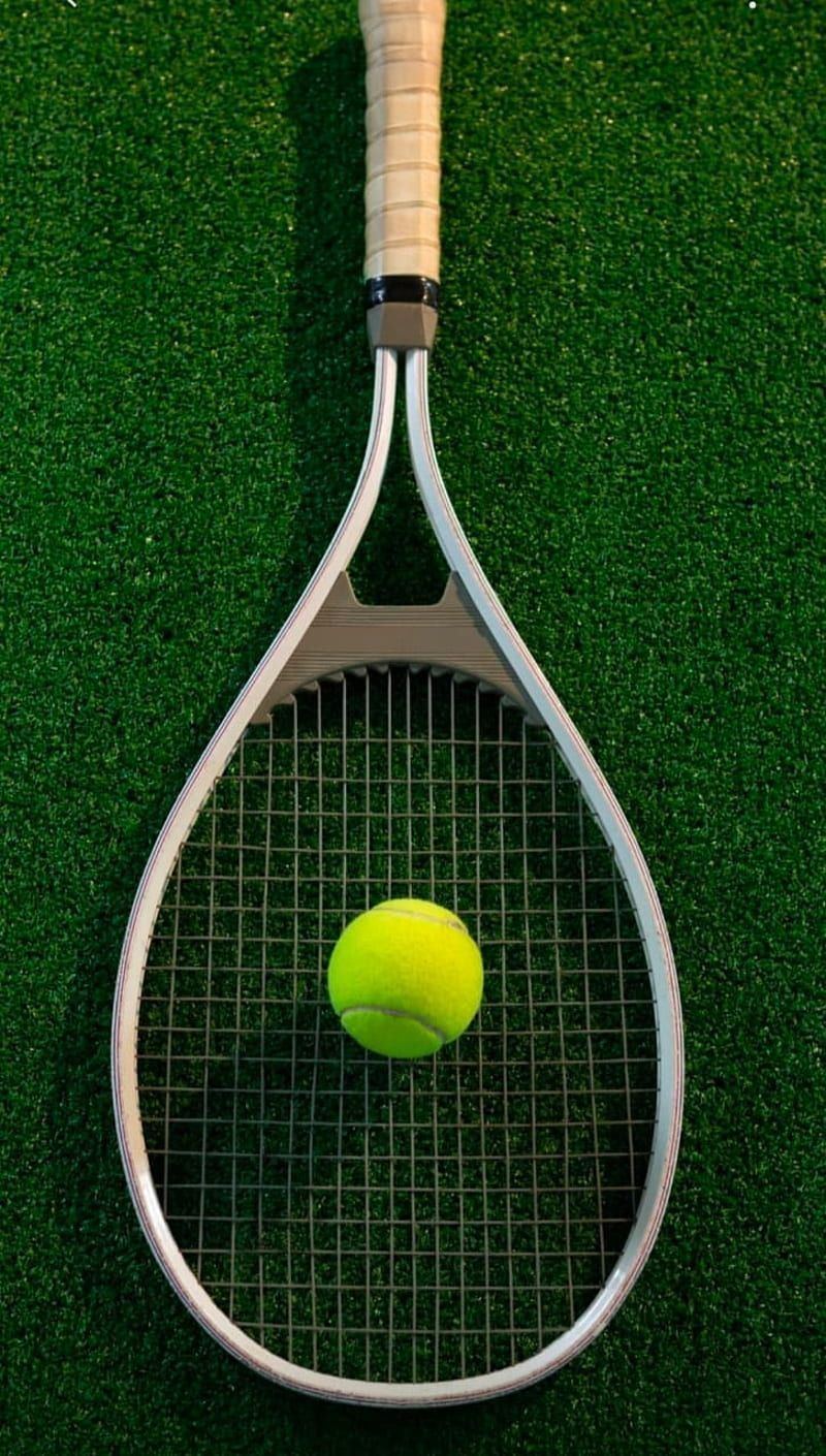 A tennis ball sits on top of a tennis racket on a grass court. - Tennis