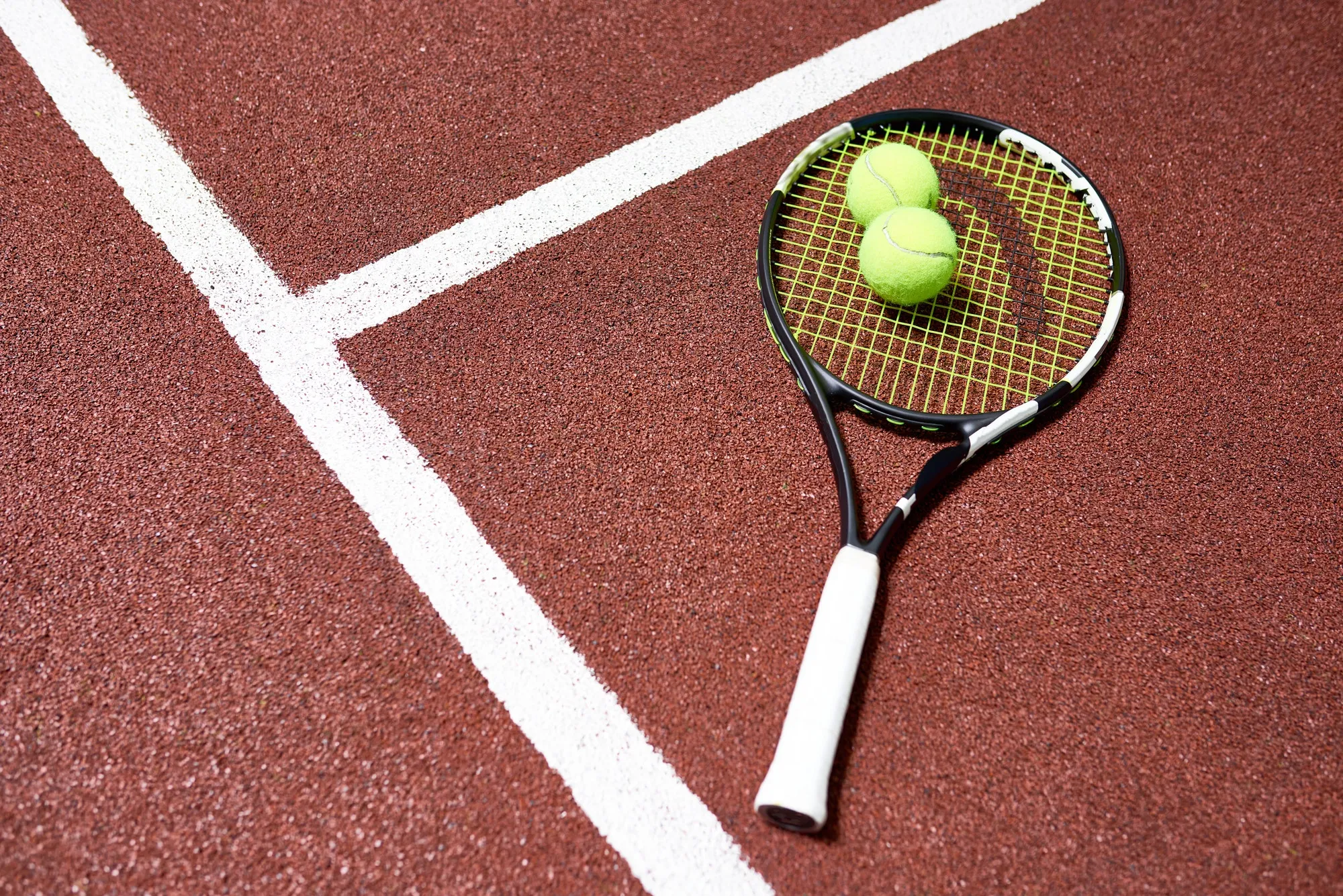A tennis racket and two tennis balls on a tennis court - Tennis