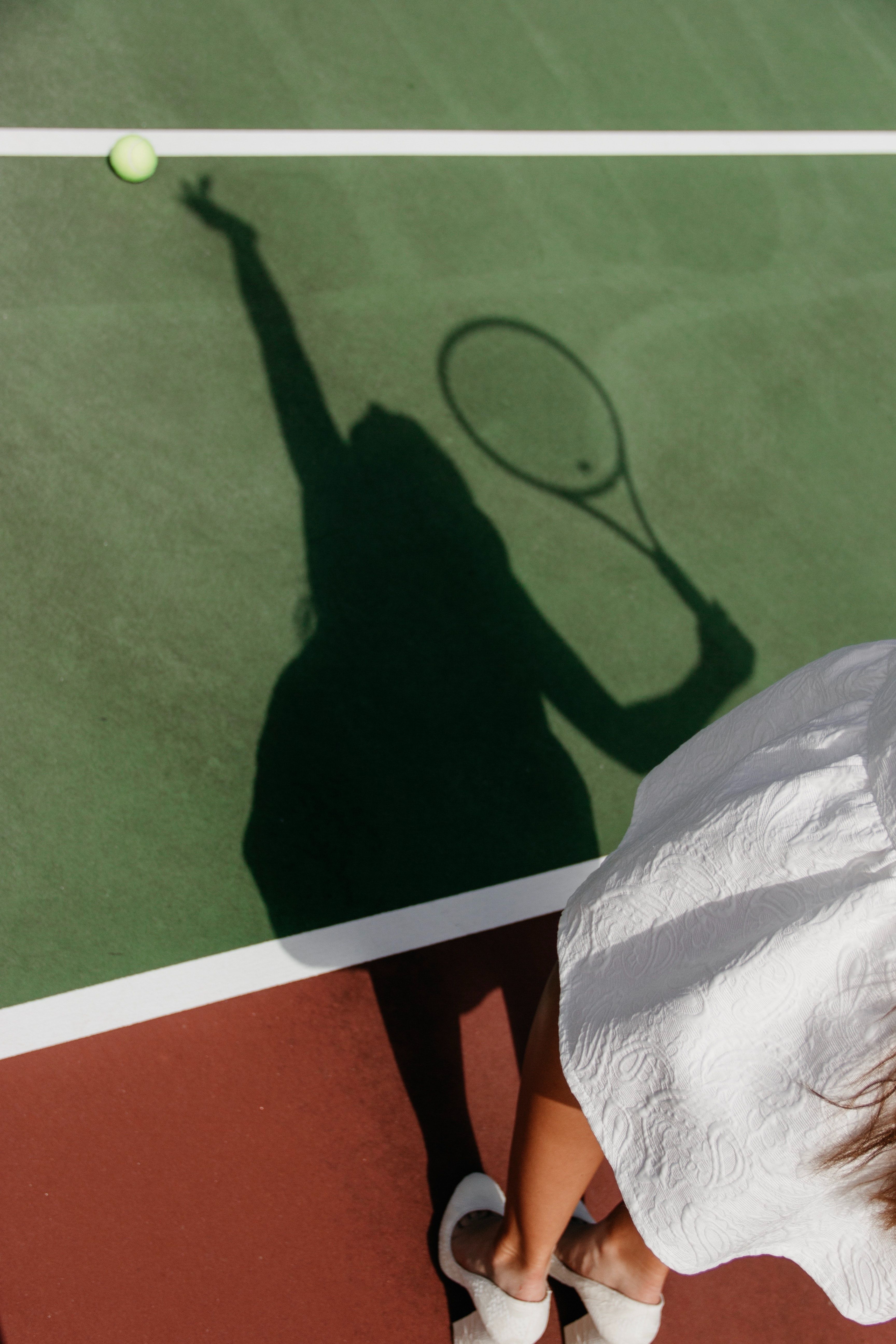 A woman playing tennis with her shadow on the court - Tennis