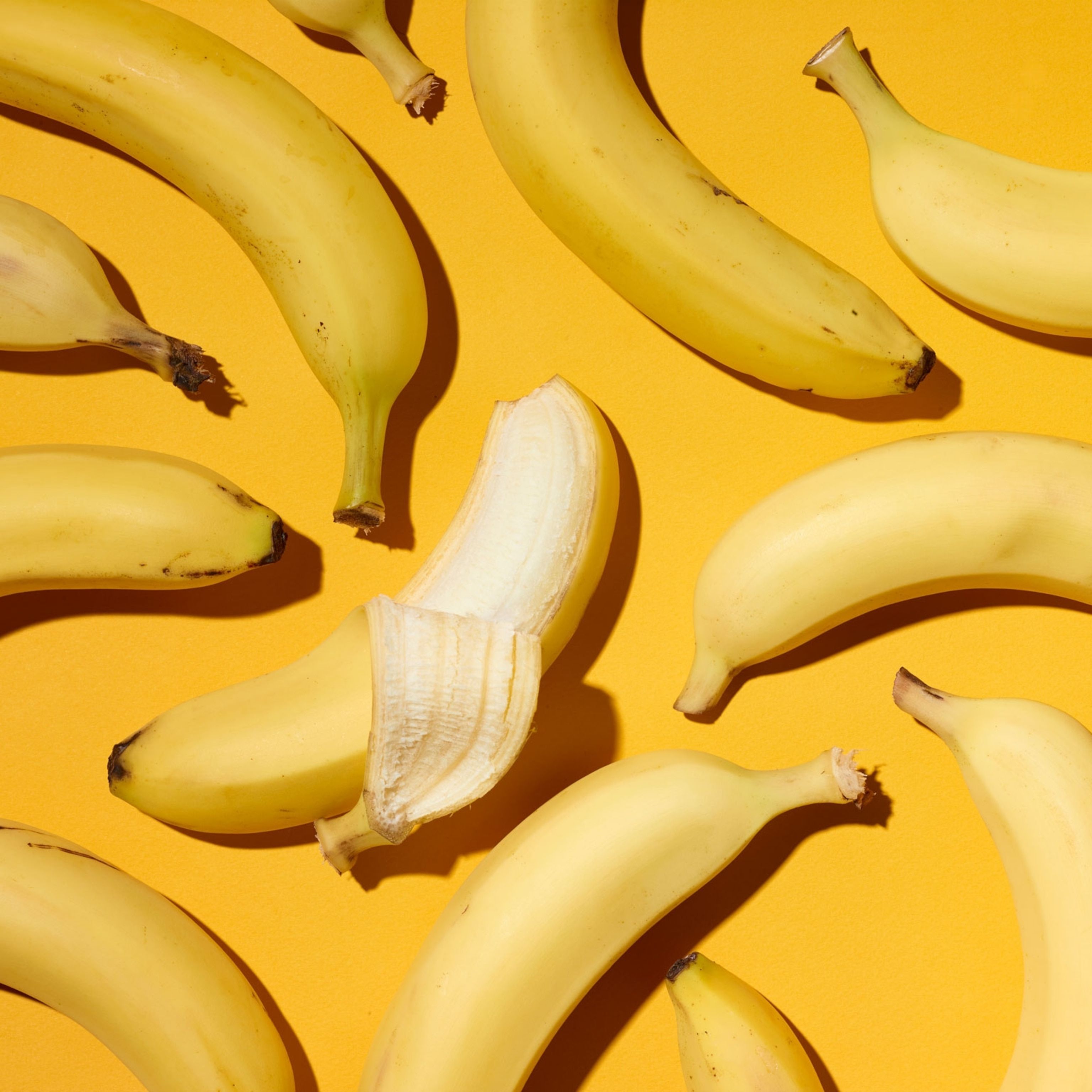 A bunch of bananas, with one peeled, on a yellow background. - Banana