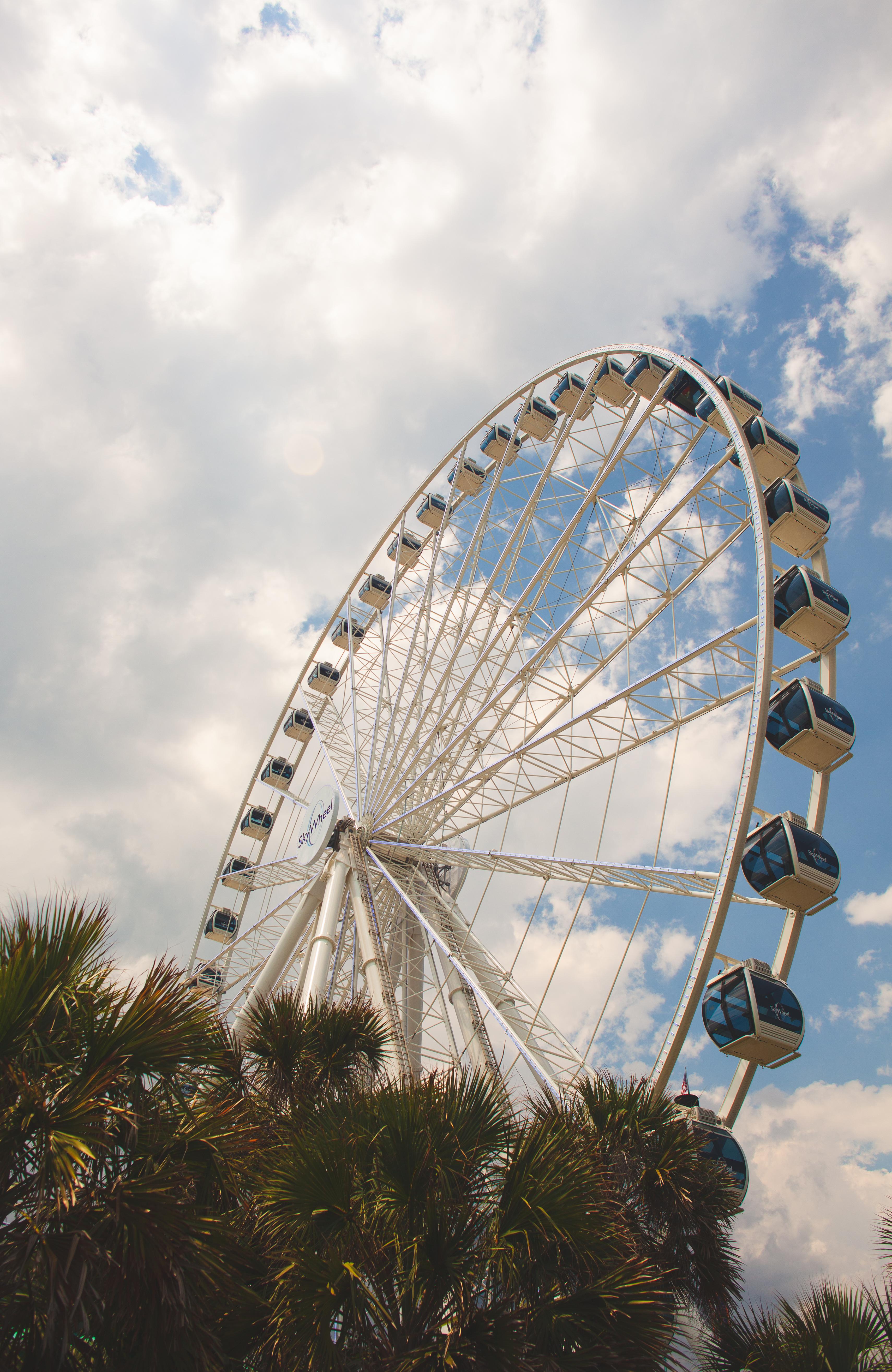 A white Ferris wheel with blue cabins against a cloudy sky. - Florida