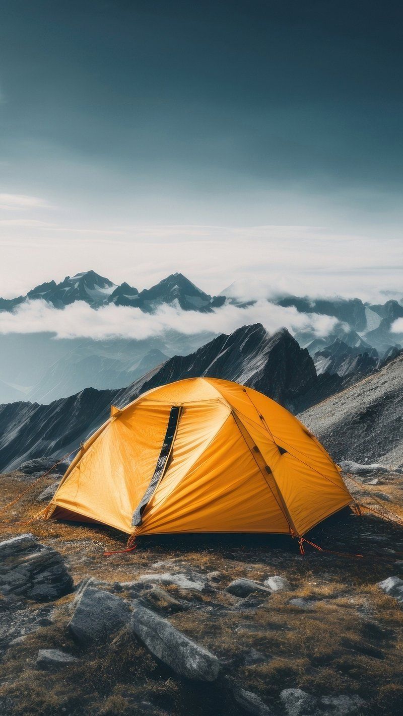 A yellow tent pitched on a rocky hillside with mountains in the background - Camping